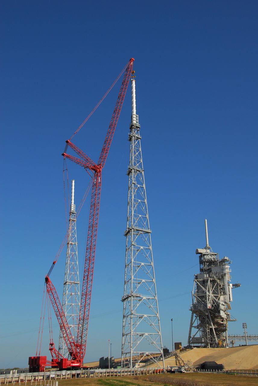 CAPE CANAVERAL, Fla. – On Launch Pad 39B at NASA's Kennedy Space Center in Florida, a giant crane places the 100-foot lightning mast on top of the newly erected lightning tower, one of three around the pad.  Another of the towers is at left.  At right are the fixed and rotating service structures that serve the Space Shuttle Program.  The new lightning protection system is being built for the Constellation Program and Ares/Orion launches.  Each of the towers is 500 feet tall with an additional 100-foot fiberglass mast atop supporting a wire catenary system.  This improved lightning protection system allows for the taller height of the Ares I rocket compared to the space shuttle.  Pad 39B will be the site of the first Ares vehicle launch, including the Ares I-X test flight that is targeted for July 2009. Photo credit: NASA/Tim Jacobs