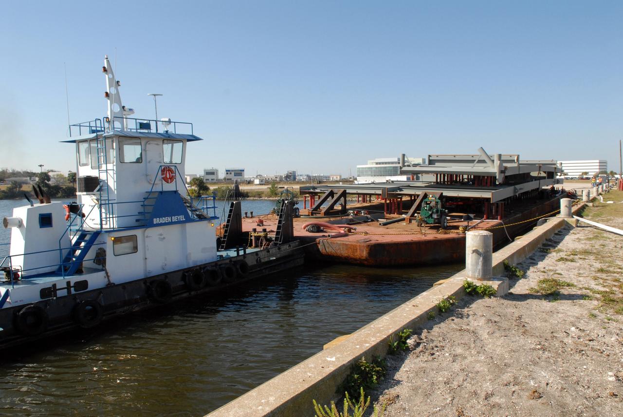 CAPE CANAVERAL, Fla. – At the turn basin at NASA's Kennedy Space Center in Florida, a tug boat keeps the barge in place for the offloading of the girder for the new mobile launcher.  The new mobile launcher will be the base for the Ares rockets to launch the Orion crew exploration vehicle and the cargo vehicle.  The base is being made lighter than space shuttle mobile launcher platforms so the crawler-transporter can pick up the added load of the 345-foot tower and taller rocket.  When the structural portion of the new mobile launcher is complete, umbilicals, access arms, communications equipment and command/control equipment will be installed.  Photo credit: NASA/Jack Pfaller