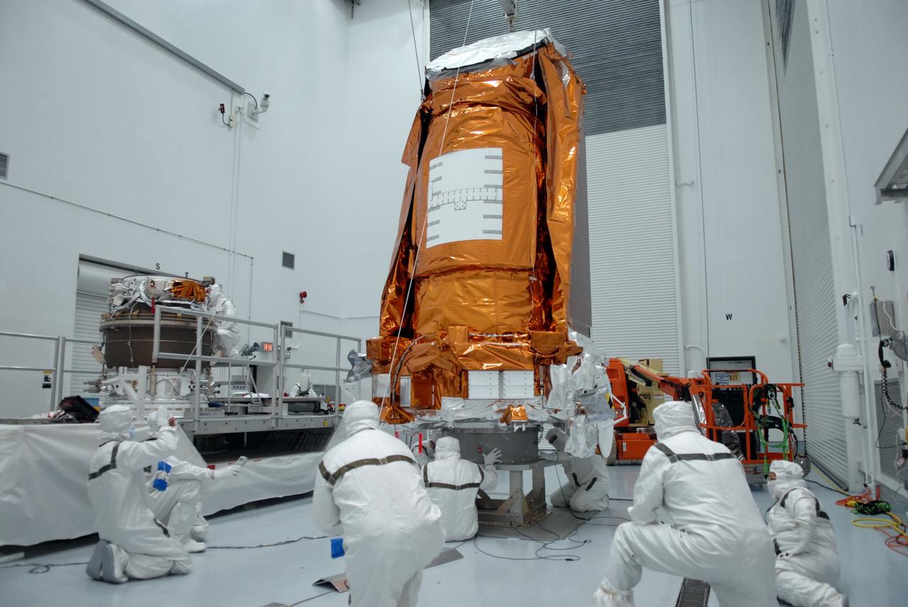 CAPE CANAVERAL, Fla. – At the Hazardous Processing Facility at Astrotech in Titusville, Fla., workers prepare to lift the Kepler spacecraft from a work stand to a Delta II third stage, at left. Kepler is designed to survey more than 100,000 stars in our galaxy to determine the number of sun-like stars that have Earth-size and larger planets, including those that lie in a star's "habitable zone," a region where liquid water, and perhaps life, could exist. If these Earth-size worlds do exist around stars like our sun, Kepler is expected to be the first to find them and the first to measure how common they are. The liftoff of Kepler aboard a Delta II rocket is currently targeted for 10:48 p.m. EST March 5 from Space Launch Complex 17 on Cape Canaveral Air Force Station. Photo credit: NASA/Troy Cryder