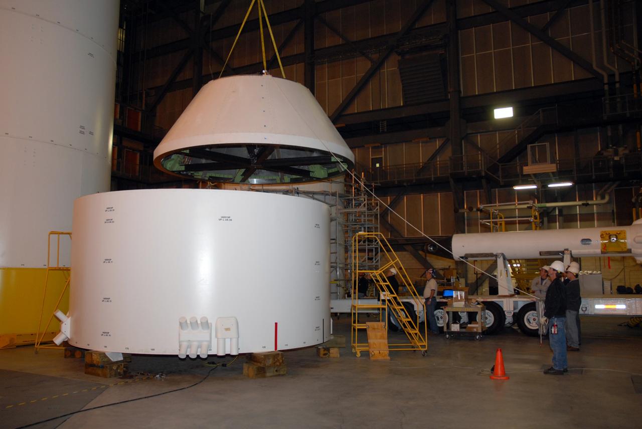 CAPE CANAVERAL, Fla. – In high bay 4 of the Vehicle Assembly Building at NASA's Kennedy Space Center, workers lower the Ares I-X crew module mock-up onto a mock-up of the service module during a fit check of the hardware. When fully developed, the 16-foot diameter crew module will furnish living space and reentry protection for future astronauts, and the service module’s main engine will be used to break out of lunar orbit for the return trip to Earth. Ares I-X is the test flight for the Ares I, which is part of the Constellation Program to return men to the moon and beyond. The I-X flight will provide NASA an early opportunity to test and prove hardware, facilities and ground operations associated with Ares I launches. Targeted for the summer of 2009, the launch of the full-scale Ares I-X will be the first in a series of unpiloted rocket launches from Kennedy. Photo credit: NASA/Jack Pfaller