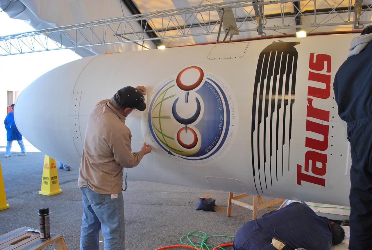 VANDENBERG AIR FORCE BASE, Calif. --  On Space Launch Complex 576-E at Vandenberg Air Force Base in California, a worker applies a mission decal to NASA's Orbiting Carbon Observatory, or OCO, spacecraft.  The spacecraft is scheduled for launch aboard Orbital Sciences' Taurus XL rocket Feb. 24 from Vandenberg. The spacecraft will collect precise global measurements of carbon dioxide (CO2) in the Earth's atmosphere. Scientists will analyze OCO data to improve our understanding of the natural processes and human activities that regulate the abundance and distribution of this important greenhouse gas.  Photo credit: NASA/Randy Beaudoin, VAFB