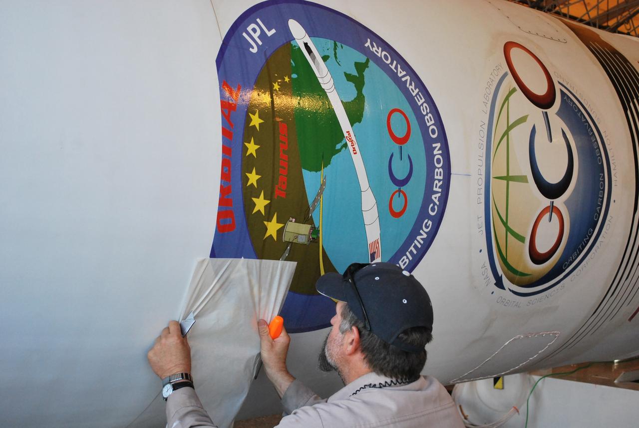 VANDENBERG AIR FORCE BASE, Calif. --  On Space Launch Complex 576-E at Vandenberg Air Force Base in California, a worker applies a mission decal to NASA's Orbiting Carbon Observatory, or OCO.  The spacecraft is scheduled for launch aboard Orbital Sciences' Taurus XL rocket Feb. 24 from Vandenberg. The spacecraft will collect precise global measurements of carbon dioxide (CO2) in the Earth's atmosphere. Scientists will analyze OCO data to improve our understanding of the natural processes and human activities that regulate the abundance and distribution of this important greenhouse gas.  Photo credit: NASA/Randy Beaudoin, VAFB