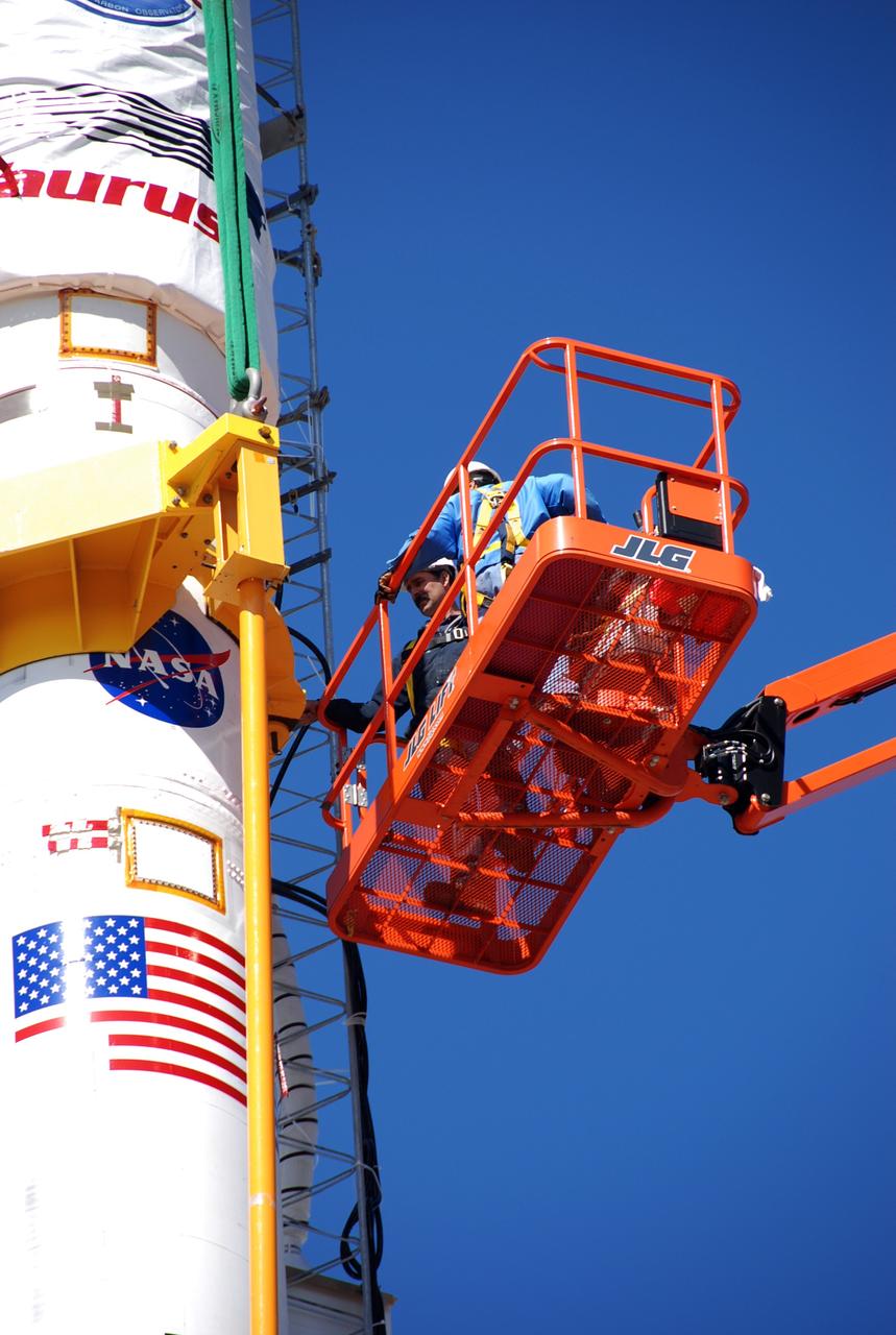 VANDENBERG AIR FORCE BASE, Calif. -- On Launch Complex 576-E at Vandenberg Air Force Base in California, Orbital Sciences Engineer Jose Castillo (right) maneuvers the bucket truck into position over the fairing access door on NASA's Orbiting Carbon Observatory, or OCO. Technician Mark Neuse feels for the payload access door through the environmental cover. OCO is scheduled for launch the Taurus rocket Feb. 24 from Vandenberg. The spacecraft will collect precise global measurements of carbon dioxide (CO2) in the Earth's atmosphere. Scientists will analyze OCO data to improve our understanding of the natural processes and human activities that regulate the abundance and distribution of this important greenhouse gas. Photo credit: NASA/Richard Nielsen, VAFB