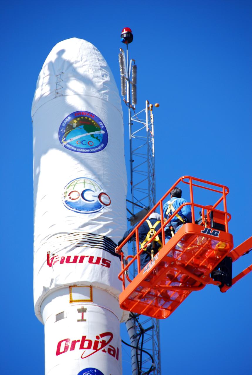 VANDENBERG AIR FORCE BASE, Calif. --  On Launch Complex 576-E at Vandenberg Air Force Base in California, Orbital Sciences Engineer Jose Castillo maneuvers the bucket truck into position over the fairing access door on NASA's Orbiting Carbon Observatory, or OCO.  On the top of the OCO fairing is the shadow of Glenn Weigle of Orbital Satellite Systems Group, on a bucket out of camera range at left, who is waiting to move in and inspect the GN2 instrument purge flow. OCO will collect precise global measurements of carbon dioxide (CO2) in the Earth's atmosphere. Scientists will analyze OCO data to improve our understanding of the natural processes and human activities that regulate the abundance and distribution of this important greenhouse gas.  Photo credit: NASA/Richard Nielsen, KSC