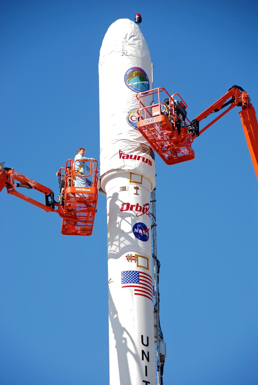 VANDENBERG AIR FORCE BASE, Calif. --  On Launch Complex 576-E at Vandenberg Air Force Base in California, Orbital Sciences Engineer Jose Castillo maneuvers the bucket truck  at right into position over the fairing access door on NASA's Orbiting Carbon Observatory, or OCO.  Glenn Weigle of Orbital Satellite Systems Group is on the bucket at left.  Weigle is prepared to move in and inspect the GN2 instrument purge flow.  OCO will collect precise global measurements of carbon dioxide (CO2) in the Earth's atmosphere. Scientists will analyze OCO data to improve our understanding of the natural processes and human activities that regulate the abundance and distribution of this important greenhouse gas. OCO is scheduled to launch Feb. 24 aboard an Orbital Sciences' Taurus XL rocket.  Photo credit: NASA/Richard Nielsen, KSC