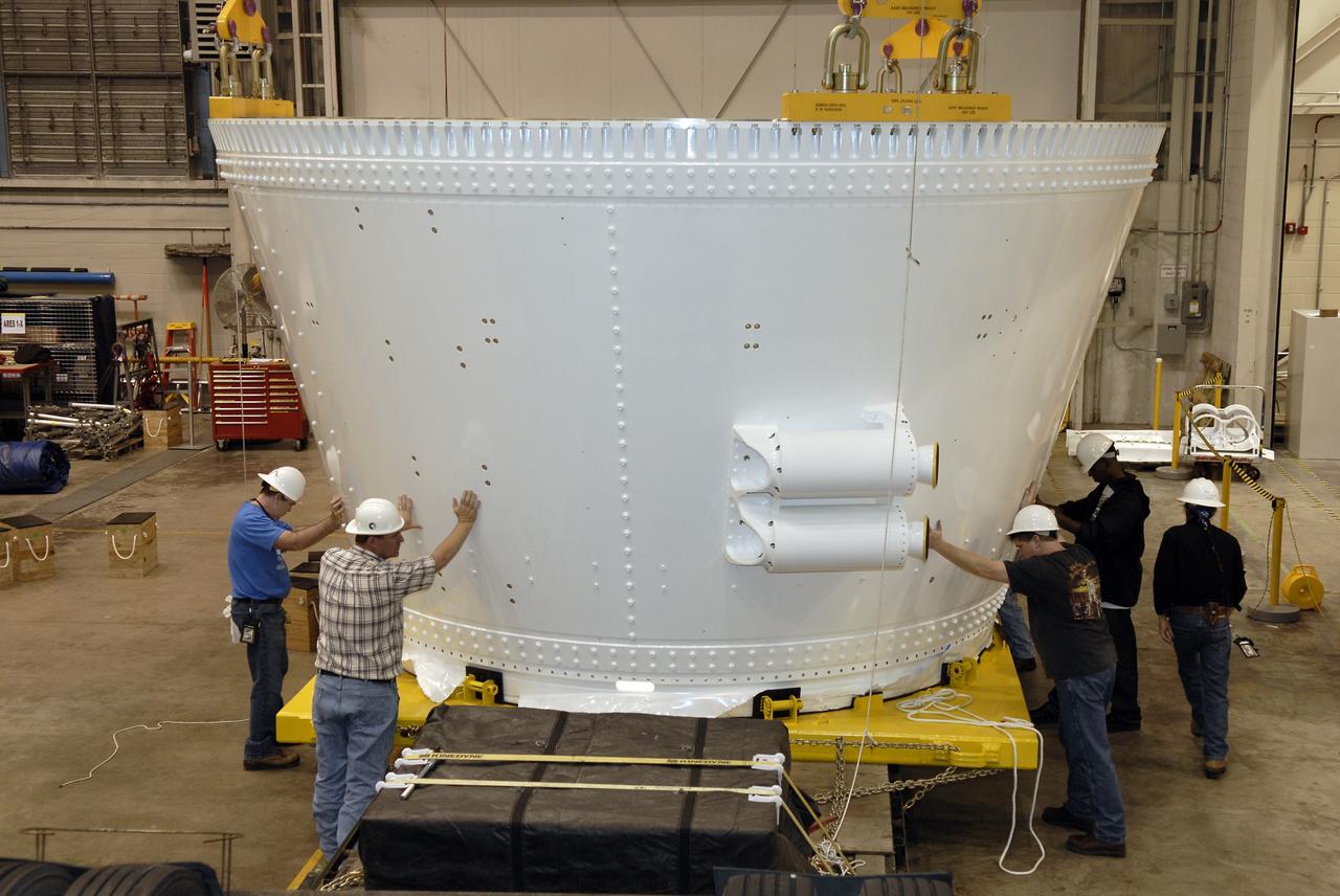 CAPE CANAVERAL, Fla. – In the Assembly and Refurbishment Facility, or ARF, at NASA's Kennedy Space Center, workers help guide the frustum as a cable lifts it from the transporter.  The last manufactured section of the Ares I-X test rocket, the frustum will be moved from the transporter to supports on the floor.  Resembling a giant funnel, the frustum's function is to transition the primary flight loads from the rocket's upper stage to the first stage. The frustum is located between the forward skirt extension and the upper stage of the Ares I-X.  The frustum will be integrated with the forward skirt and forward skirt extension, which already are in the ARF. That will complete the forward assembly. The assembly then will be moved to the Vehicle Assembly Building for stacking operations, which are scheduled to begin in April.  Photo credit: NASA/Kim Shiflett