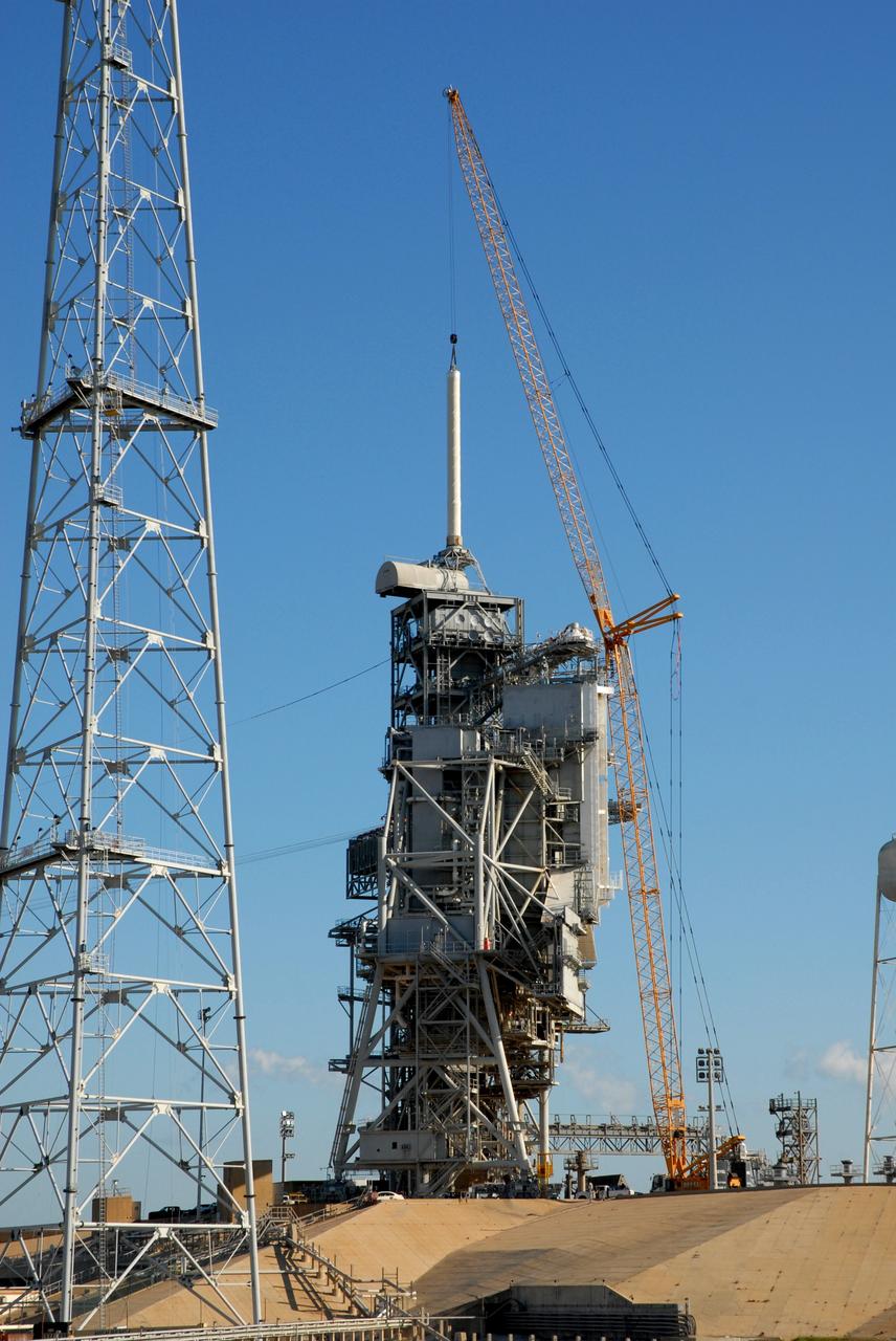 CAPE CANAVERAL, Fla. – On Launch Pad 39B at NASA's Kennedy Space Center in Florida, a crane is being used to remove the 80-foot lightning mast from the top of the fixed service structure.  The mast is no longer needed with the erection of the three lightning towers around the pad.  Pad 39B will be the site of the first Ares vehicle launch, including the Ares I-X test flight that is targeted for July 2009.  The three new lightning towers are 500 feet tall with an additional 100-foot fiberglass mast atop supporting a wire catenary system.  This improved lightning protection system allows for the taller height of the Ares I rocket compared to the space shuttle.  Photo credit: NASA/Amanda Diller