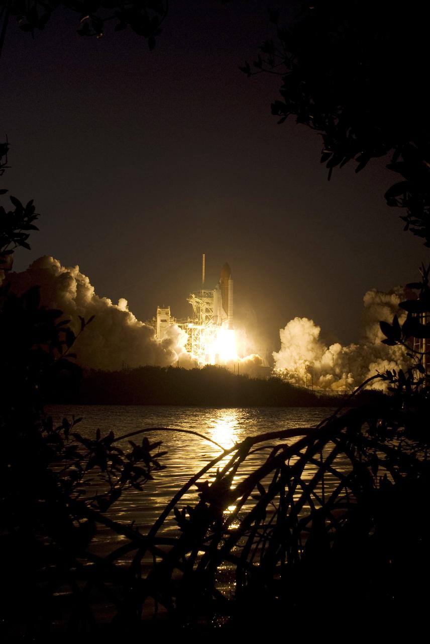 CAPE CANAVERAL, Fla. – Viewed across the water near Launch Pad 39A at NASA's Kennedy Space Center in Florida, launch of space shuttle Discovery on the STS-119 mission spews fire into the night. The launch was on time at 7:43 p.m. EDT.  The STS-119 mission is the 28th to the International Space Station and the 125th space shuttle flight.  Discovery will deliver the final pair of power-generating solar array wings and the S6 truss segment.  Installation of S6 will signal the station's readiness to house a six-member crew for conducting increased science. Photo credit: NASA/Sandra Joseph, Kevin O'Connell