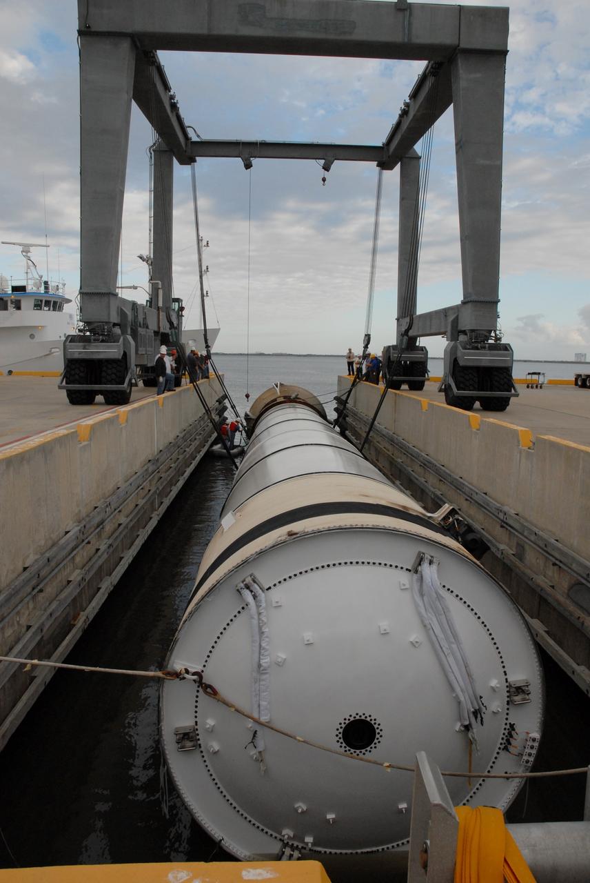 CAPE CANAVERAL, Fla. – At the dock at Hangar AF at Cape Canaveral Air Force Station in Florida, one of the  solid rocket boosters used during space shuttle Discovery's launch March 15 on mission STS-119 is moved to an area beneath the straddle crane that will lift it out of the water.  The space shuttle’s solid rocket booster casings and associated flight hardware are recovered at sea after a launch. The spent rockets were recovered by NASA's Solid Rocket Booster Retrieval Ships Freedom Star and Liberty Star. The boosters impact the Atlantic Ocean approximately seven minutes after liftoff.  The splashdown area is a square of about six by nine nautical miles located about 140 nautical miles downrange from the launch pad. The retrieval ships are stationed approximately 8 to 10 nautical miles from the impact area at the time of splashdown. As soon as the boosters enter the water, the ships accelerate to a speed of 15 knots and quickly close on the boosters. The pilot chutes and main parachutes are the first items to be brought on board. With the chutes and frustum recovered, attention turns to the boosters. The ship’s tow line is connected and the booster is returned to the Port and, after transfer to a position alongside the ship, to Hangar AF. There, the expended boosters are disassembled, refurbished and reloaded with solid propellant for reuse.  Photo credit: NASA/Jack Pfaller