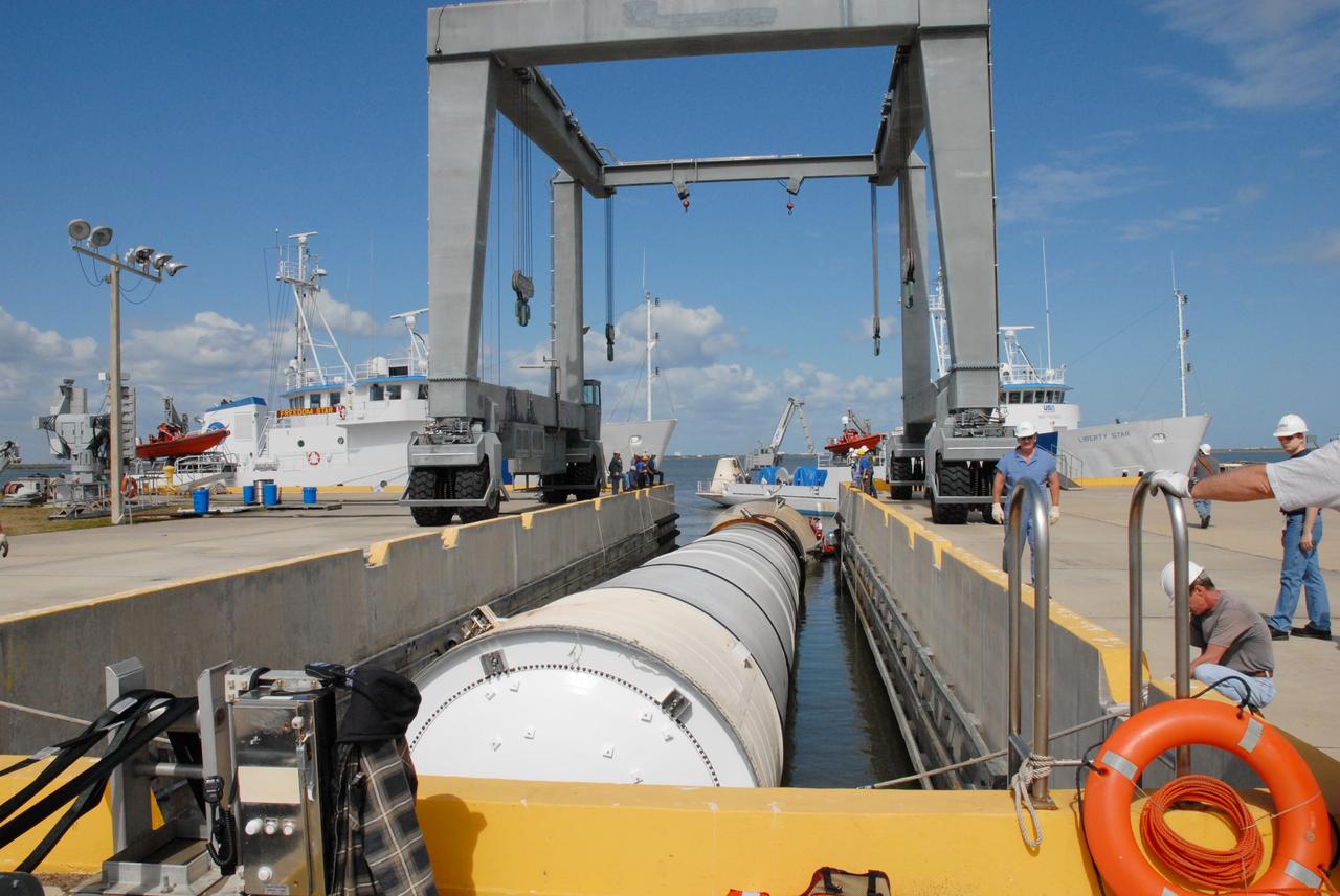 CAPE CANAVERAL, Fla. – At the dock at Hangar AF at Cape Canaveral Air Force Station in Florida, a solid rocket boosters used during space shuttle Discovery's launch from NASA's Kennedy Space Center in Florida March 15 on mission STS-119 waits in an area beneath the straddle crane that will lift it out of the water. The space shuttle’s solid rocket booster casings and associated flight hardware are recovered at sea after a launch. The spent rockets were recovered by NASA's Solid Rocket Booster Retrieval Ships Freedom Star and Liberty Star. The boosters impact the Atlantic Ocean approximately seven minutes after liftoff.  The splashdown area is a square of about six by nine nautical miles located about 140 nautical miles downrange from the launch pad. The retrieval ships are stationed approximately 8 to 10 nautical miles from the impact area at the time of splashdown. As soon as the boosters enter the water, the ships accelerate to a speed of 15 knots and quickly close on the boosters. The pilot chutes and main parachutes are the first items to be brought on board. With the chutes and frustum recovered, attention turns to the boosters. The ship’s tow line is connected and the booster is returned to the Port and, after transfer to a position alongside the ship, to Hangar AF. There, the expended boosters are disassembled, refurbished and reloaded with solid propellant for reuse.  Photo credit: NASA/Jack Pfaller