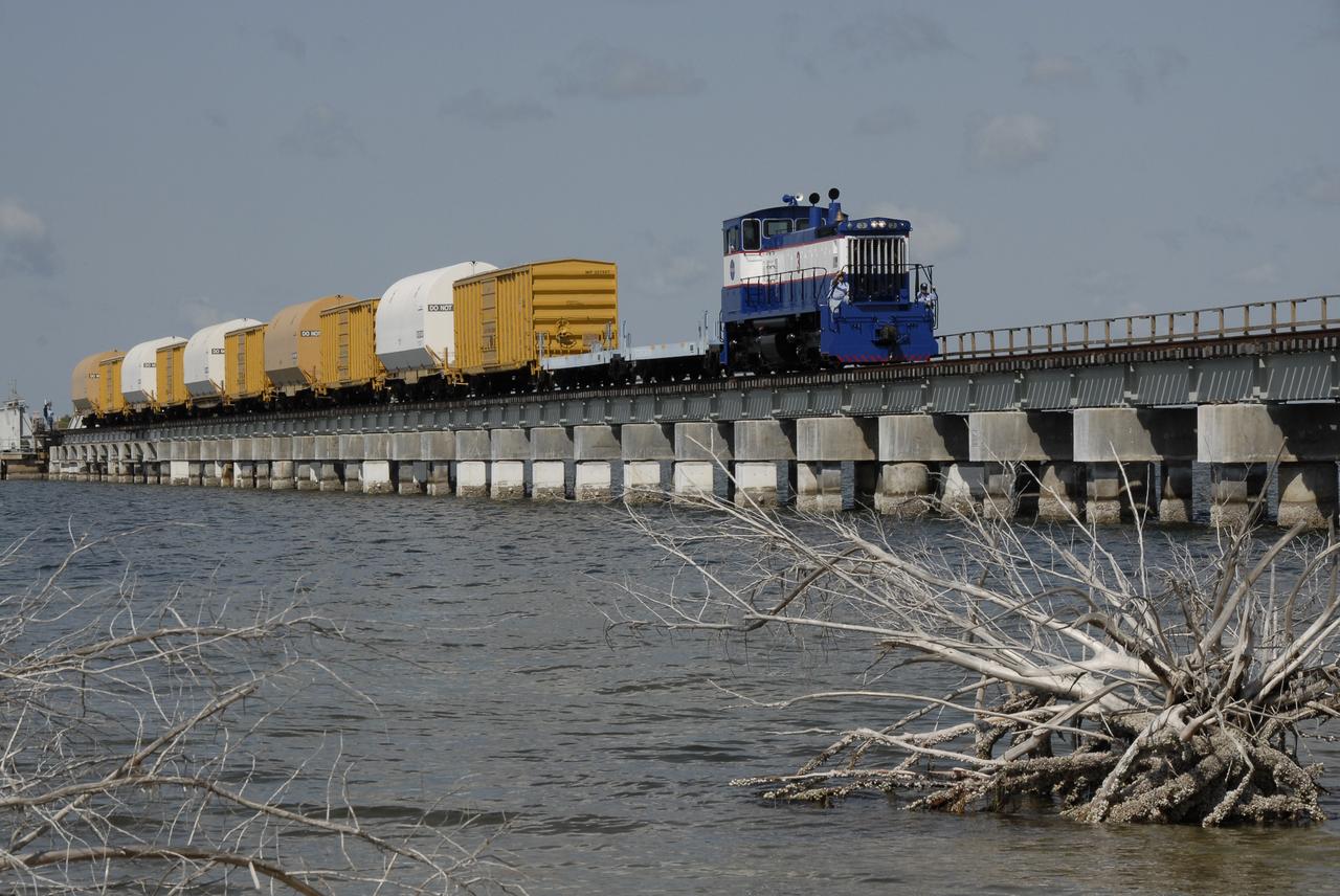 CAPE CANAVERAL, Fla. – The NASA Railroad hauls cars carrying the Ares I-X motor segments and nozzle exit cone over a river bridge to NASA's Kennedy Space Center in Florida.  The four reusable motor segments and the nozzle exit cone, manufactured by the Ares I first-stage prime contractor Alliant Techsystems Inc., or ATK, departed Utah March 12 on the seven-day, cross-country trip to Florida.  The segments will be delivered to Kennedy's  Rotation, Processing and Surge Facility for final processing and integration. The booster used for the Ares I-X launch is being modified by adding new forward structures and a fifth segment simulator. The motor is the final hardware needed for the rocket's upcoming test flight this summer. The stacking operations are scheduled to begin in the Vehicle Assembly Building in April.   Photo credit: NASA/Kim Shiflett