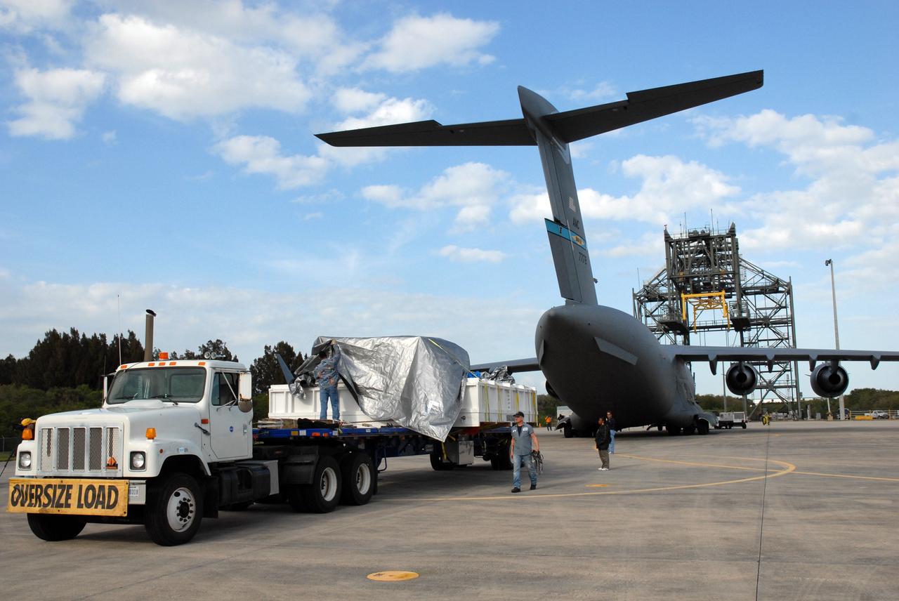CAPE CANAVERAL, Fla. – On the Shuttle Landing Facility at NASA's Kennedy Space Center in Florida, a worker removes a cover from the EXPRESS Logistics Carrier for the STS-129 mission.  The truck and carrier arrived on the C-17 cargo plane in the background. The carrier is part of the payload on space shuttle Atlantis, which will deliver to the International Space Station components including two spare gyroscopes, two nitrogen tank assemblies, two pump modules, an ammonia tank assembly and a spare latching end effector for the station's robotic arm.  STS-129 is targeted to launch Nov. 12.  Photo credit: NASA/Tim Jacobs