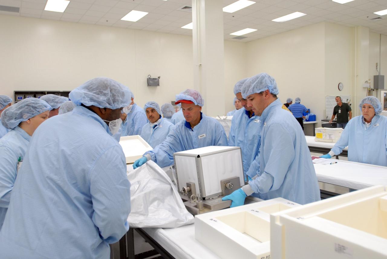 CAPE CANAVERAL, Fla. – In the Space Station Processing Facility, STS-128 crew members look over packages of equipment that will accompany the mission.  At center (with the red cap) is Commander Rick Sturckow; to his left is Mission Specialist José Hernandez.  The STS-128 flight will carry science and storage racks to the International Space Station on space shuttle Discovery. Launch of Discovery is targeted for Aug. 6.  Photo credit: NASA/Jim Grossmann