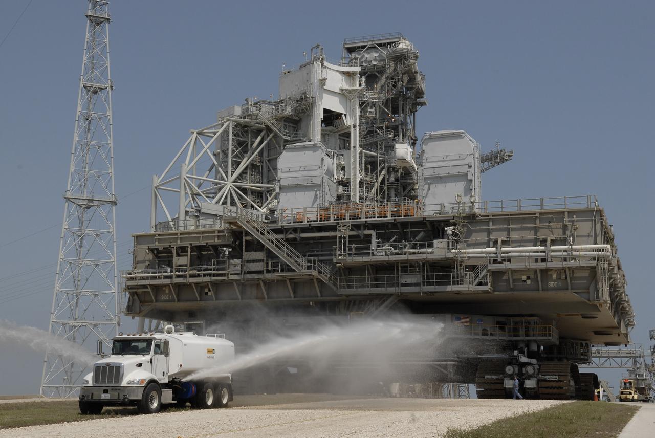 CAPE CANAVERAL, Fla. – At NASA's Kennedy Space Center in Florida, a water truck sprays the dry crawlerway in front of the crawler-transporter carrying the mobile launcher platform on top as it moves away from Kennedy's Launch pad 39B.  The platform, turned over from the shuttle program to the Constellation Program last month, will be rolled into the Vehicle Assembly Building's High Bay 3 in preparation for the Ares I-X flight test this summer. Ares I-X is the test vehicle for the Ares I, which is part of the Constellation Program to return men to the moon and beyond.  Ground Control System hardware was installed in MLP-1 in December 2008.  The platform was moved to the launch pad to check out the installed hardware with the Launch Control Center Firing Room 1 equipment, using the actual circuits that will be used when the fully stacked Ares I-X vehicle is rolled out later this year for launch.  Photo credit: NASA/Kim Shiflett