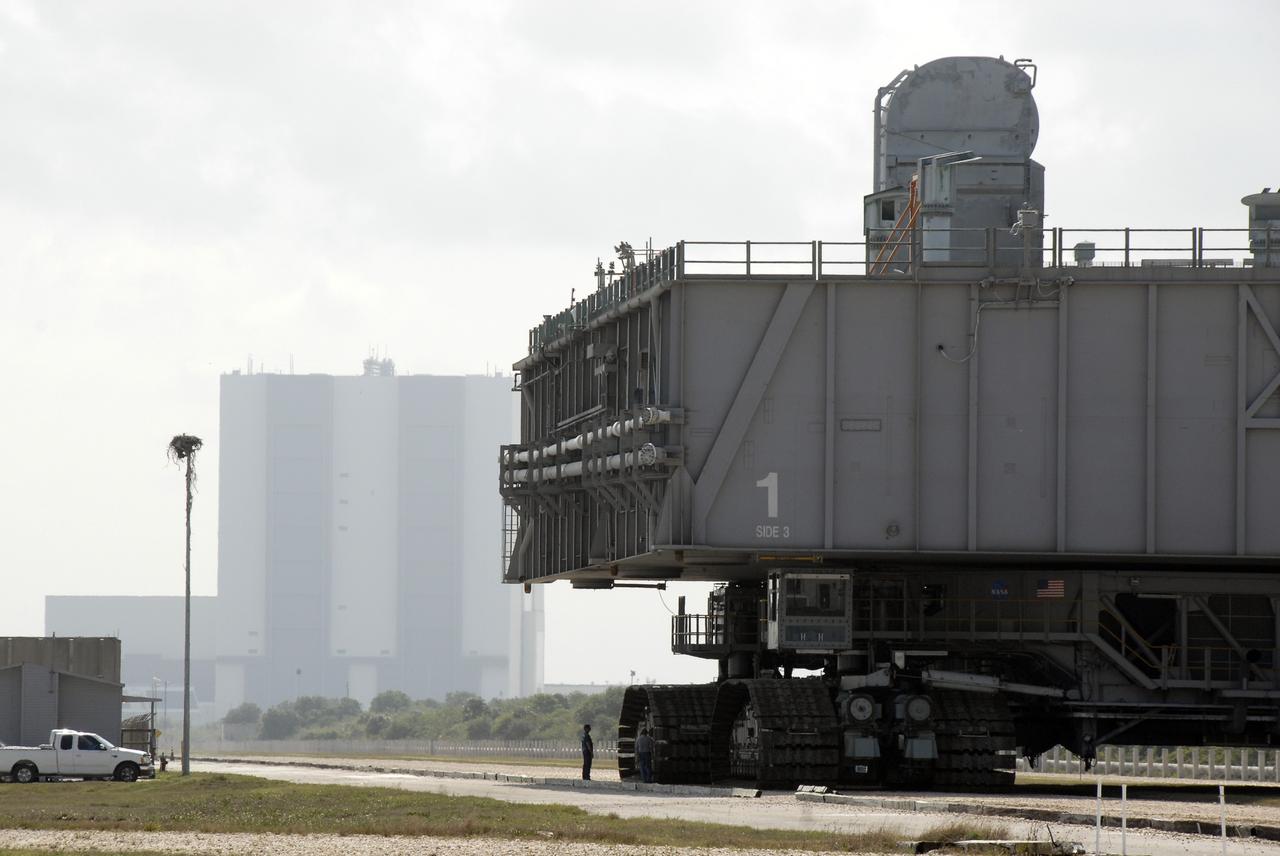 CAPE CANAVERAL, Fla. – A worker is dwarfed by the giant crawler-transporter and mobile launcher platform moving along the crawlerway toward the Vehicle Assembly Building. The platform will be rolled into the VAB's High Bay 3 in preparation for the Ares I-X flight test this summer.  Ares I-X is the test vehicle for the Ares I, which is part of the Constellation Program to return men to the moon and beyond.  Ground Control System hardware was installed in MLP-1 in December 2008.  The platform was moved to the launch pad to check out the installed hardware with the Launch Control Center Firing Room 1 equipment, using the actual circuits that will be used when the fully stacked Ares I-X vehicle is rolled out later this year for launch.  Photo credit: NASA/Kim Shiflett