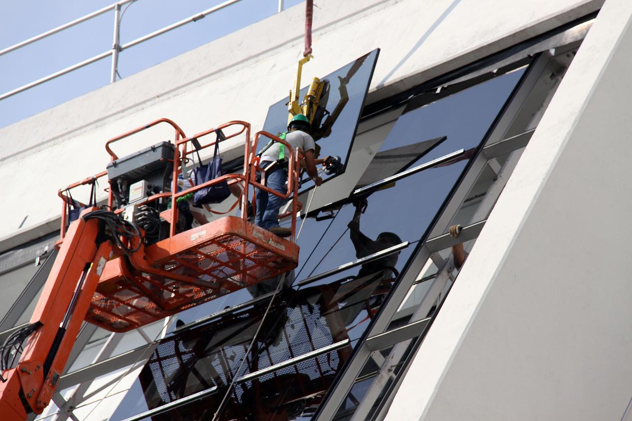 CAPE CANAVERAL, Fla. –  A new window is lowered toward the existing Firing Room windows in the Launch Control Center at NASA's Kennedy Space Center in Florida. New, hurricane-rated window systems for the four Firing Rooms and the vestibule areas between Firing Rooms 1 & 2 and Firing Rooms 3 & 4 are being installed. In order to avoid operational impacts the new windows are being installed on the outside of the existing windows, enclosing the space formerly occupied by the louvers.  The old windows will remain in place until the new windows are completely installed and leak tested. This approach will continue to keep the firing rooms from being exposed to the elements.   Photo credit: NASA/Jack Pfaller
