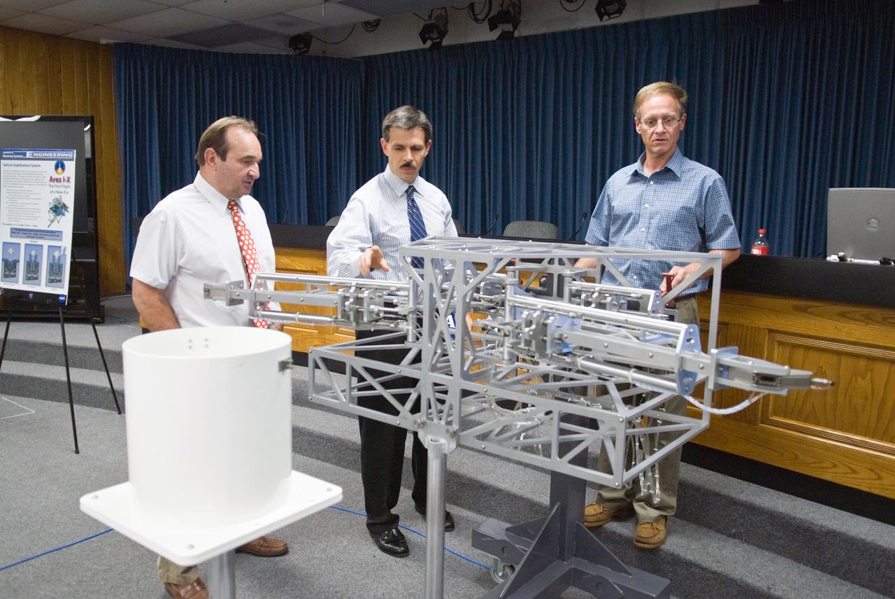 CAPE CANAVERAL, Fla. –  In the NASA News Center TV Studio at NASA's Kennedy Space Center in Florida, on view is a 1/12 model of the vehicle stabilization system that will be installed on Launch Pad 39B to hold the Ares I-X rocket for its flight test.  Looking at the model are (from left) Roger Lenard, consultant with Lee & Associates, LCC; Jon Cowart, NASA's Ares I-X deputy mission manager; and Eric Mellberg, Ares I-X Vehicle Stabilization Design lead with United Space Alliance Ares I-X is the test vehicle for the Ares I, which is part of the Constellation Program to return men to the moon and beyond. Ares I-X is targeted for launch in August 2009.  Photo credit: NASA/Kim Shiflett