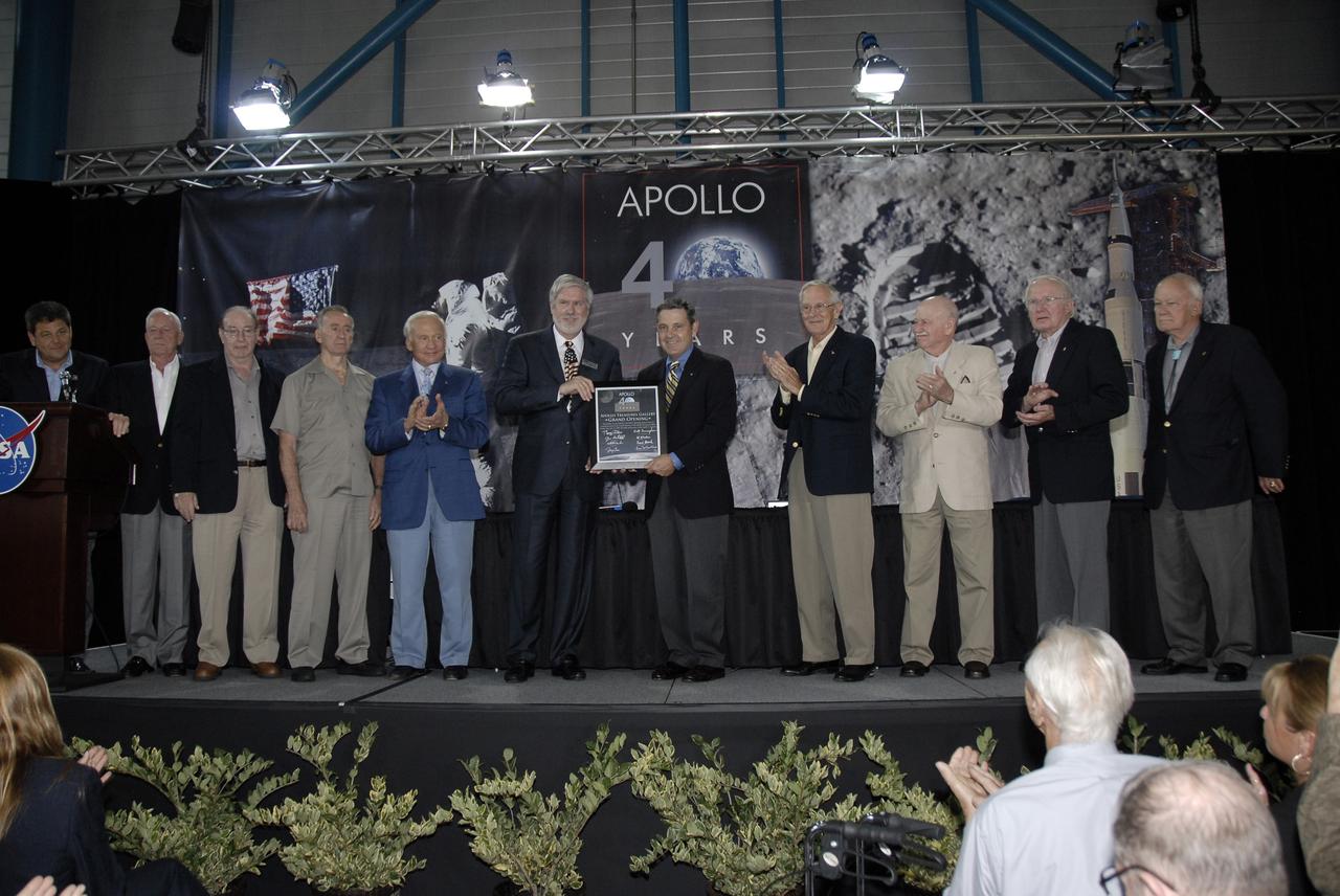 CAPE CANAVERAL, Fla. – During NASA's 40th Anniversary of Apollo Celebration at the Apollo/Saturn V Center at NASA's Kennedy Space Center in Florida, the Visitor Complex Chief Operating Officer, Bob Moore (center left), gives Center Director Bob Cabana a plaque commemorating the Apollo Treasures Gallery.  Others on stage are (far left) the program moderator, John Zarella, with CNN, and Apollo astronauts Al Worden, Edgar Mitchell, Walt Cunningham, Buzz Aldrin, (Moore, Cabana), Charlie Duke, Vance Brand, Gerald Carr and Bruce McCandless. The celebration honored the July 1969 launch and landing on the moon.  Photo credit: NASA/Kim Shiflett