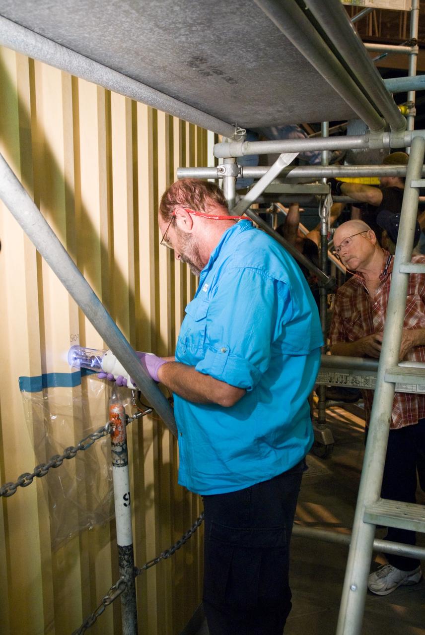CAPE CANAVERAL, Fla. – In the Vehicle Assembly Building's  High Bay 1 at NASA's Kennedy Space Center in Florida, David Buras, a Material and Process engineer from NASA's Michoud Assembly Facility near New Orleans where external fuel tanks are built, is testing foam adhesion on the intertank of space shuttle Discovery's  external tank. He is collecting foam samples an inch-and-half in diameter for analysis to confirm the foam is bonded well to the metal primer underneath.  At right is Jerrol Kinsey, a NASA quality inspector. The testing was prompted by the foam loss during launch of space shuttle Endeavour on the STS-127 mission July 15. Samples are being sent to Michoud for study.  Photo credit: NASA/Tim Jacobs
