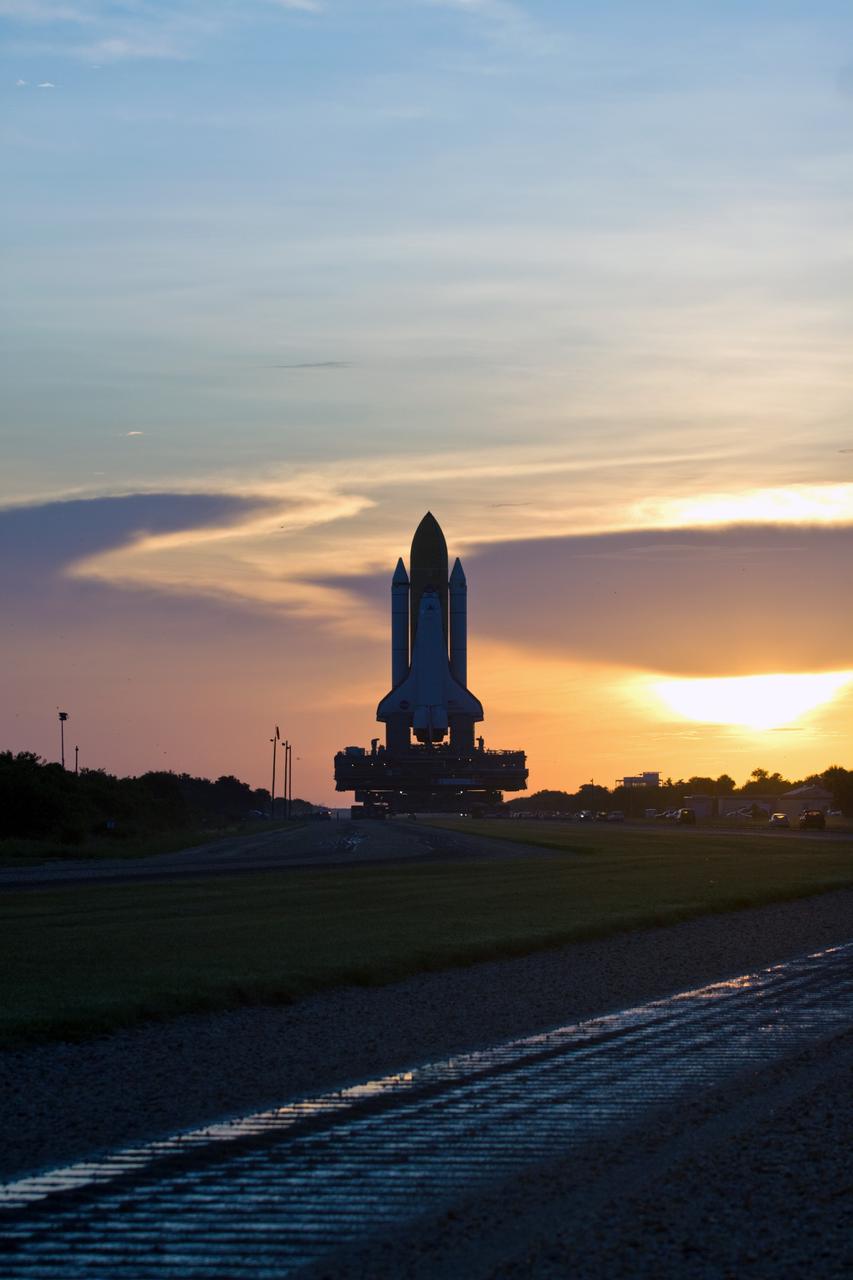 CAPE CANAVERAL, Fla. – Space shuttle Discovery is silhouetted against the dawn sky as it rolls out to Launch Pad 39A at NASA's Kennedy Space Center in Florida. The 3.4-mile journey was slower than usual as technicians stopped several times to clear mud from the crawler's treads and bearings. The waterlogged crawlerway can be seen in the foreground. First motion out of the Vehicle Assembly Building was at 2:07 a.m. EDT Aug. 4. Rollout was delayed approximately 2 hours due to lightning in the area. Discovery's 13-day flight will deliver a new crew member and 33,000 pounds of equipment to the International Space Station. The equipment includes science and storage racks, a freezer to store research samples, a new sleeping compartment and the COLBERT treadmill. Launch of Discovery on its STS-128 mission is targeted for late August. Photo credit: NASA/Dimitri Gerondidakis