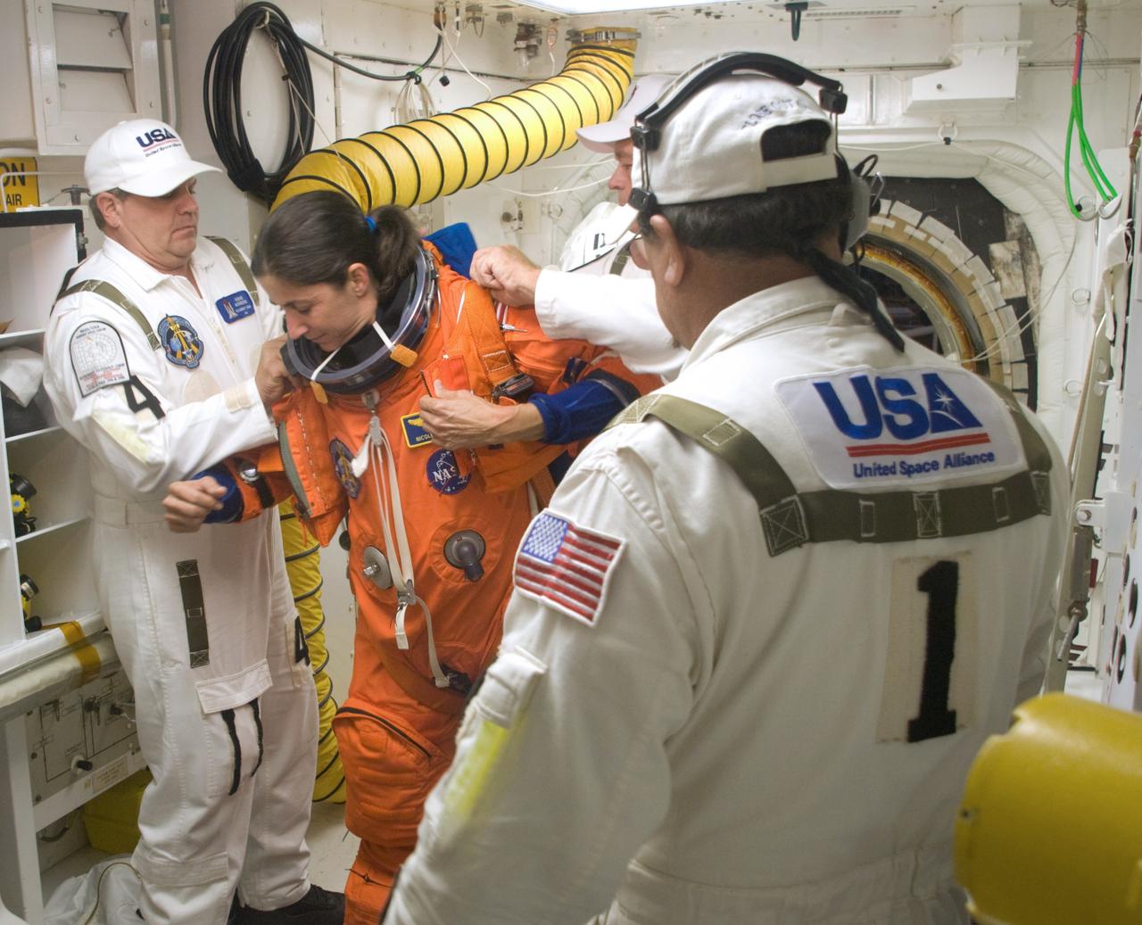 CAPE CANAVERAL, Fla. – In the White Room on NASA Kennedy Space Center's Launch Pad 39A, STS-128 Mission Specialist Nicole Stott is helped getting into her parachute harness before entering space shuttle Discovery. The White Room is at the end of the orbiter access arm and provides entry into the shuttle. The crew is at Kennedy to take part in the terminal countdown demonstration test, or TCDT, which includes equipment familiarization, emergency exit training and a simulated countdown. On the STS-128 mission, Discovery will deliver 33,000 pounds of equipment to the station, including science and storage racks, a freezer to store research samples, a new sleeping compartment and the COLBERT treadmill.  Launch is targeted for late August.  Photo credit: NASA/Kim Shiflett