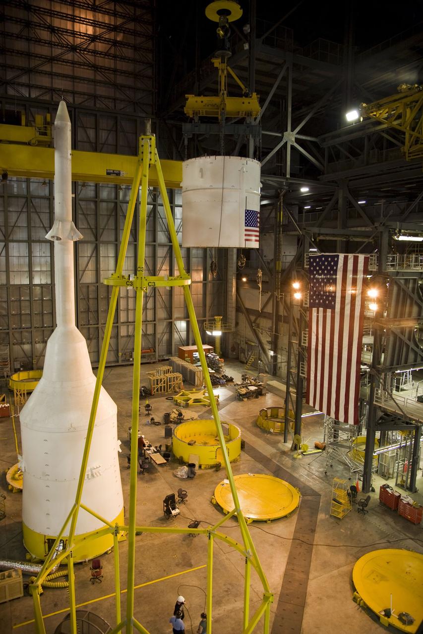 CAPE CANAVERAL, Fla. – In the Vehicle Assembly Building's High Bay 4 at NASA's Kennedy Space Center in Florida, a crane begins moving the Ares I-X Super Stack 4 to High Bay 3 for integration with Super Stack 3.  At left are the crew module-launch abort system and simulator service module-service adapter stack and  the "birdcage," the special crane that will lift the stack.  Five super stacks make up the upper stage that will be integrated with the four-segment solid rocket booster first stage on the mobile launch platform.  Ares I-X is the test vehicle for the Ares I, which is part of the Constellation Program to return men to the moon and beyond. The Ares I-X flight test is targeted for  Oct. 31, pending formal NASA Headquarters approval. Photo credit: NASA/Dimitri Gerondidakis