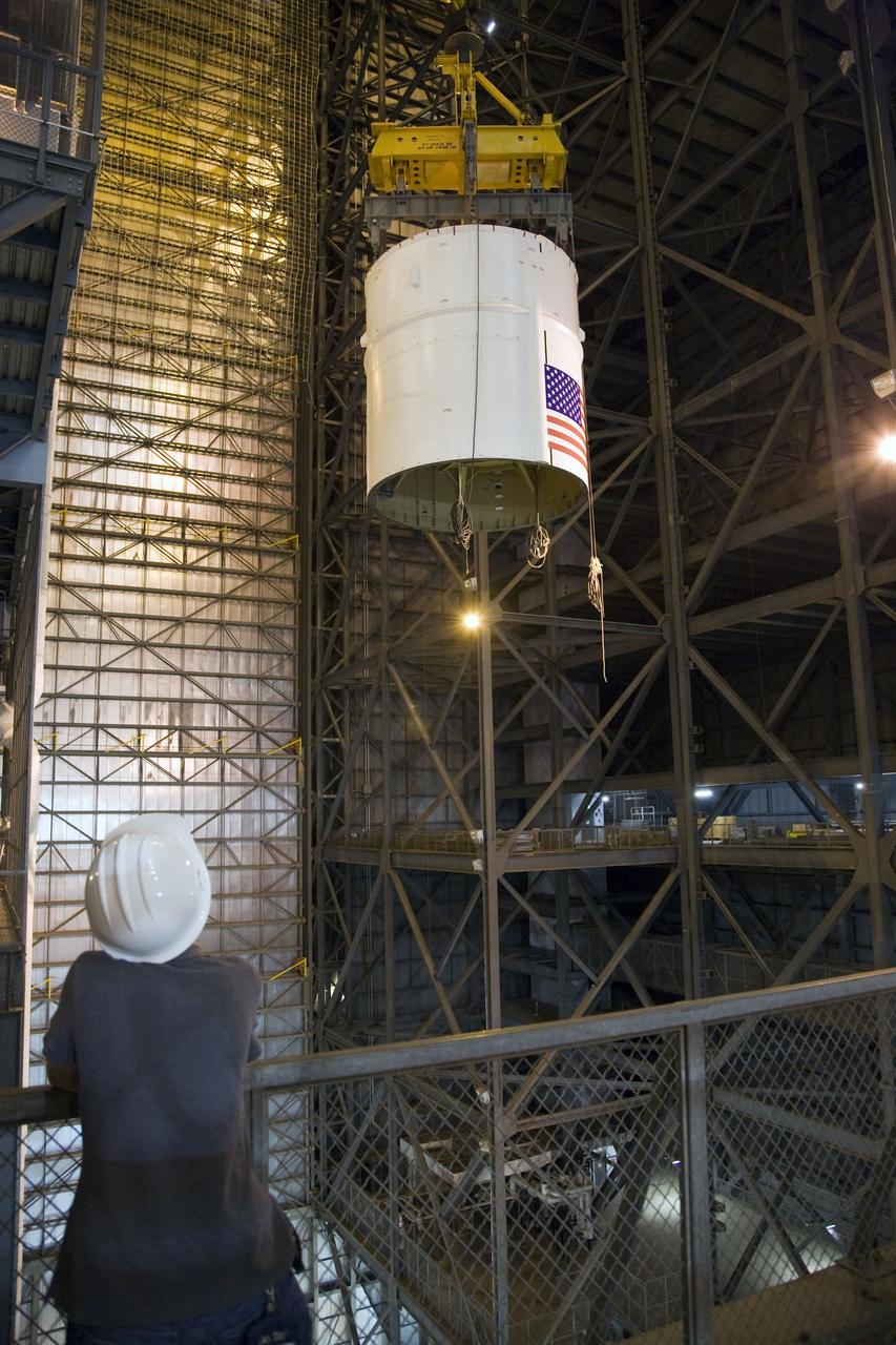 CAPE CANAVERAL, Fla. – In the Vehicle Assembly Building's High Bay 3, a worker watches as a crane lowers the Ares I-X Super Stack 4 for integration with Super Stack 3. Five super stacks make up the upper stage that will be integrated with the four-segment solid rocket booster first stage on the mobile launch platform. Ares I-X is the test vehicle for the Ares I, which is part of the Constellation Program to return men to the moon and beyond. The Ares I-X flight test is targeted for Oct. 31, pending formal NASA Headquarters approval. Photo credit: NASA/Dimitri Gerondidakis