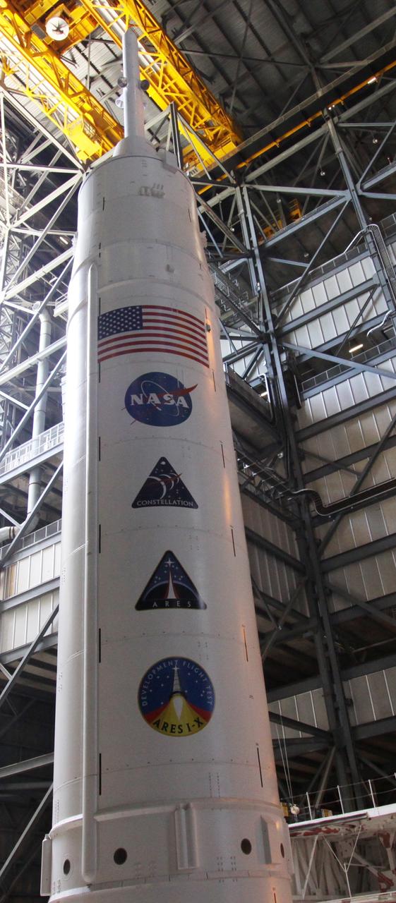 CAPE CANAVERAL, Fla. – The 327-foot tall Ares I-X rocket stretches into the upper regions of NASA Kennedy Space Center's Vehicle Assembly Building.  The rocket is stacked on the mobile launcher platform in High Bay 3.  Mission, program and NASA decals are lined up on the stack below the U.S. flag.  Five super stacks make up the upper stage that are integrated with the four-segment solid rocket booster first stage below.  Ares I-X is the test vehicle for the Ares I, which is part of the Constellation Program to return men to the moon and beyond. The Ares I-X flight test is targeted for  Oct. 31.  Photo credit: NASA/Jack Pfaller