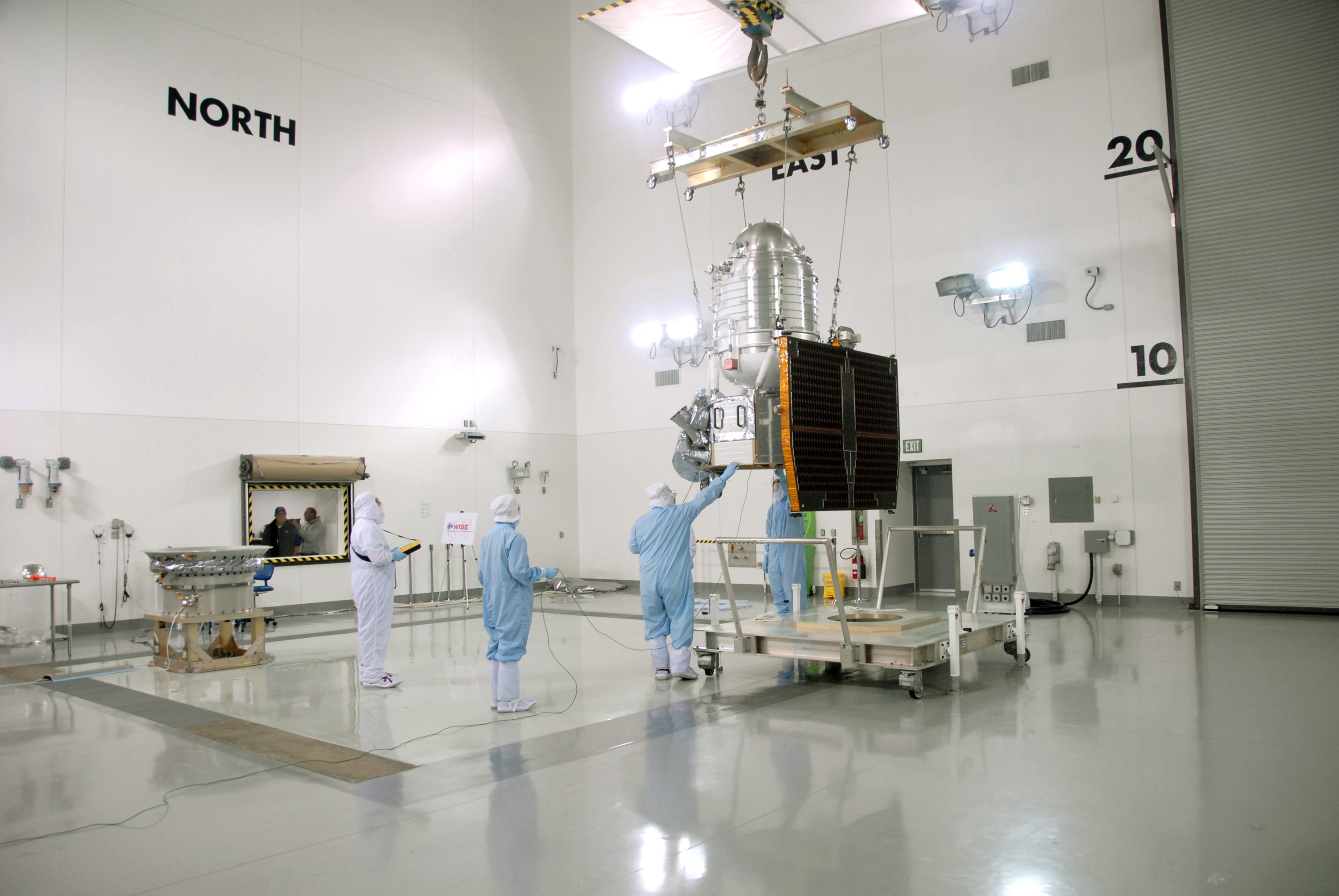 VANDENBERG AIR FORCE BASE, Calif. -- At Vandenberg Air Force Base's Astrotech processing facility in California, technicians help guide NASA's Wide-field Infrared Survey Explorer, or WISE, spacecraft to the flight conical adapter and test stand, at far left. The satellite will survey the entire sky at infrared wavelengths, creating a cosmic clearinghouse of hundreds of millions of objects, which will be catalogued, providing a vast storehouse of knowledge about the solar system, the Milky Way, and the universe. Launch is scheduled no earlier than Dec. 7. Photo credit: NASA/Doug Kolkow