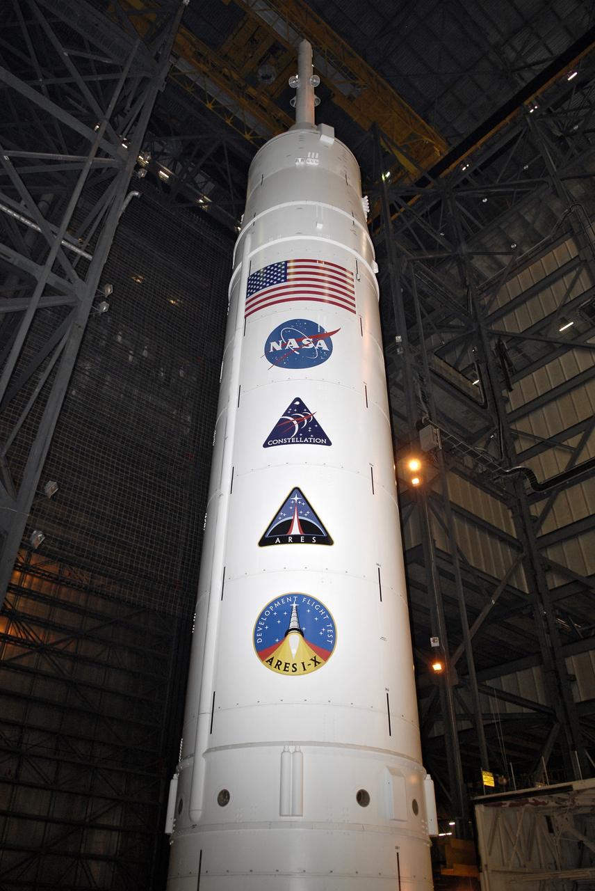 CAPE CANAVERAL, Fla. – Program and NASA decals, along with the U.S. flag, stretch the length of the Ares I-X upper stage stacked in the Vehicle Assembly Building's High Bay 4 at NASA's Kennedy Space Center in Florida. The rocket has undergone a sway test that simulated conditions the rocket could experience during rollout to Launch Pad 39B, wind conditions at the pad and first-stage ignition. During the test, vibrations are mechanically induced into the rocket by four hydraulic shakers and a sway is manually introduced for lateral motion to measure the vehicle's response. A total of 44 accelerometers are installed on the flight test vehicle that required more than 27,000 feet of cable. Part of the Constellation Program, the Ares I-X is the test vehicle for the Ares I, which is the essential core of a space transportation system that eventually will carry crewed missions back to the moon, on to Mars and out into the solar system . The Ares I-X flight test is targeted for Oct. 31. Photo credit: NASA/Kim Shiflett