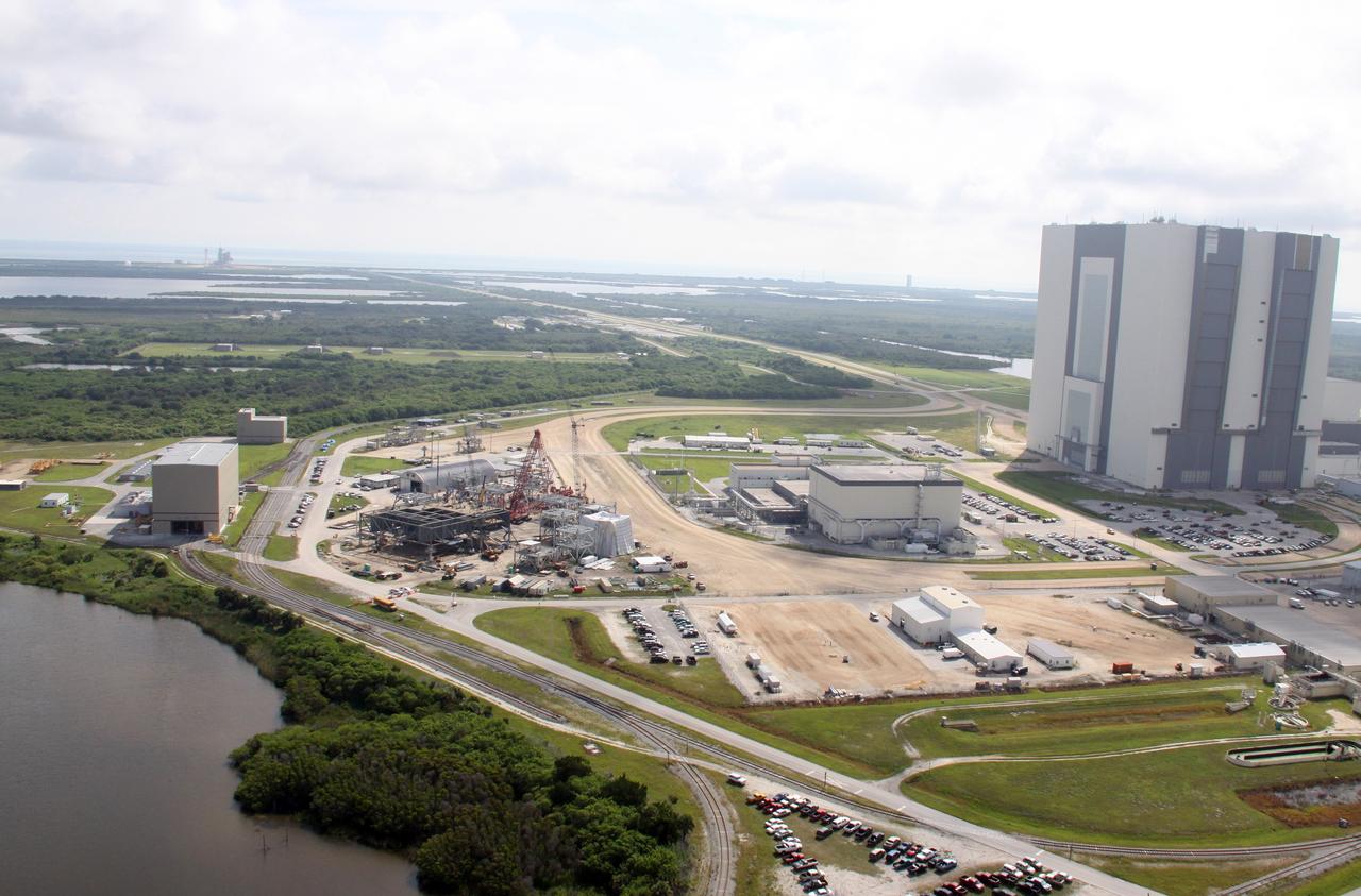 CAPE CANAVERAL, Fla. – In the mobile launcher parking area, at left, behind NASA Kennedy Space Center's Vehicle Assembly Building, at far right, the new mobile launcher, or ML, for the Ares rockets is under construction. In the background is Launch Complex 39A and the Atlantic Ocean beyond. The ML will be the base to launch the Orion crew exploration vehicle and the cargo vehicle. The base is being made lighter than space shuttle mobile launcher platforms so the crawler-transporter can pick up the added load of the 345-foot tower and taller rocket. When the structural portion of the new mobile launcher is complete, umbilicals, access arms, communications equipment and command/control equipment will be installed. Photo credit: NASA/Troy Cryder