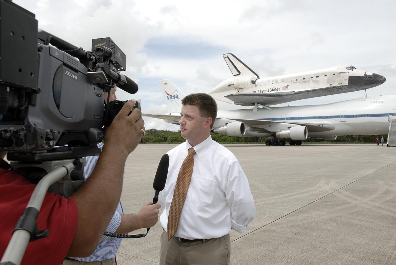 CAPE CANAVERAL, Fla. –  A reporter and videographer interview Mission Management Team Chair Mike Moses after the landing of space shuttle Discovery atop the Boeing 747 Shuttle Carrier Aircraft, in the background.  The piggybacked shuttle and aircraft landed on the Shuttle Landing Facility's runway 33 at 12:05 p.m. EDT.  The two-day return flight from Edwards Air Force Base in California began at 9:20 a.m. EDT Sept. 20.  After three fueling stops that included an overnight stay in Louisiana, the piggybacked shuttle had to navigate through a line of showers across Louisiana and around Kennedy. Discovery had landed at Edwards Sept. 11 after the 13-day STS-128 mission to the International Space Station. The shuttle delivered more than 7 tons of supplies, science racks and equipment, as well as additional environmental hardware to sustain six crew members on the station.  Landings at Kennedy were waved off on two days due to inclement weather, leading to the landing at Edwards.  Photo credit: NASA/Kim Shiflett