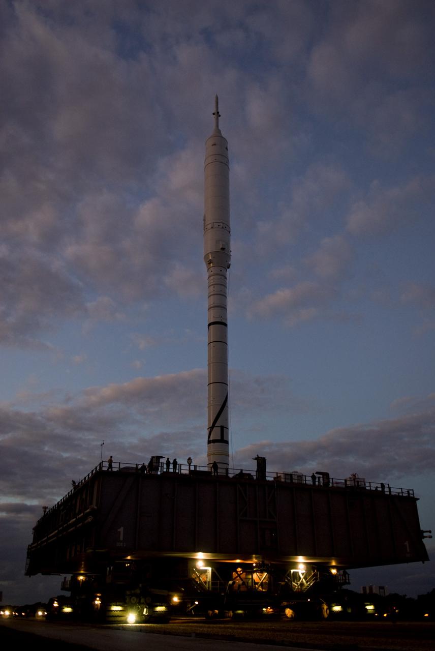 CAPE CANAVERAL, Fla. – As the sun rises over NASA's Kennedy Space Center in Florida, workers hitch a ride on the mobile launcher platform with the 327-foot-tall Ares I-X rocket, on its way to Launch Pad 39B.    The test rocket left the Vehicle Assembly Building at 1:39 a.m. EDT on its 4.2-mile trek to the pad and was "hard down" on the pad’s pedestals at 9:17 a.m.  The transfer of the pad from the Space Shuttle Program to the Constellation Program took place May 31. Modifications made to the pad include the removal of shuttle unique subsystems, such as the orbiter access arm and a section of the gaseous oxygen vent arm, along with the installation of three 600-foot lightning towers, access platforms, environmental control systems and a vehicle stabilization system.  Part of the Constellation Program, the Ares I-X is the test vehicle for the Ares I. The Ares I-X flight test is targeted for Oct. 27. For information on the Ares I-X vehicle and flight test, visit http://www.nasa.gov/aresIX.  Photo credit: NASA/Kim Shiflett
