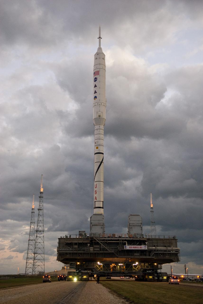 CAPE CANAVERAL, Fla. – As the sun rises over Launch Pad 39B at NASA's Kennedy Space Center in Florida, the 327-foot-tall Ares I-X rocket, secured to a mobile launcher platform, approaches the pad's perimeter fence.    The test rocket left the Vehicle Assembly Building at 1:39 a.m. EDT on its 4.2-mile trek to the pad and was "hard down" on the pad’s pedestals at 9:17 a.m.  The transfer of the pad from the Space Shuttle Program to the Constellation Program took place May 31. Modifications made to the pad include the removal of shuttle unique subsystems, such as the orbiter access arm and a section of the gaseous oxygen vent arm, along with the installation of three 600-foot lightning towers, access platforms, environmental control systems and a vehicle stabilization system.  Part of the Constellation Program, the Ares I-X is the test vehicle for the Ares I. The Ares I-X flight test is targeted for Oct. 27. For information on the Ares I-X vehicle and flight test, visit http://www.nasa.gov/aresIX.  Photo credit: NASA/Kim Shiflett