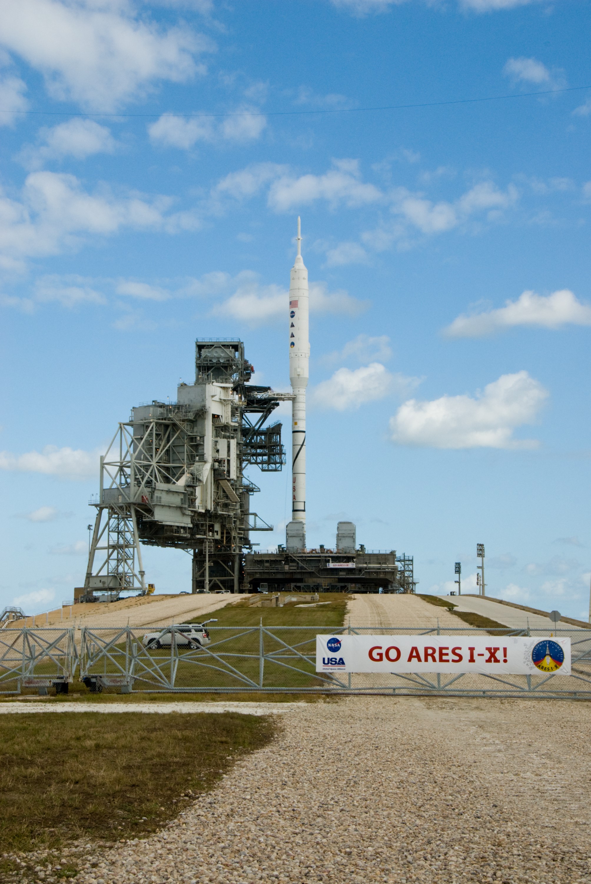 CAPE CANAVERAL, Fla. – Go Ares I-X! A banner on the perimeter fence of Launch Pad 39B at NASA's Kennedy Space Center in Florida reflects the excitement building in Kennedy's work force in anticipation of the flight test of the towering 327-foot-tall Ares I-X rocket. The test rocket left the Vehicle Assembly Building at 1:39 a.m. EDT on its 4.2-mile trek to the pad and was "hard down" on the pad’s pedestals at 9:17 a.m. A Flight Test Readiness Review, a meeting to assess preparations for the flight test, is scheduled for Oct. 23. The flight test is targeted for Oct. 27. The transfer of the pad from the Space Shuttle Program to the Constellation Program took place May 31. Modifications made to the pad include the removal of shuttle unique subsystems, such as the orbiter access arm and a section of the gaseous oxygen vent arm, along with the installation of three 600-foot lightning towers, access platforms, environmental control systems and a vehicle stabilization system. Part of the Constellation Program, the Ares I-X is the test vehicle for the Ares I. For information on the Ares I-X vehicle and flight test, visit http://www.nasa.gov/aresIX. Photo credit: NASA/Kim Shiflett