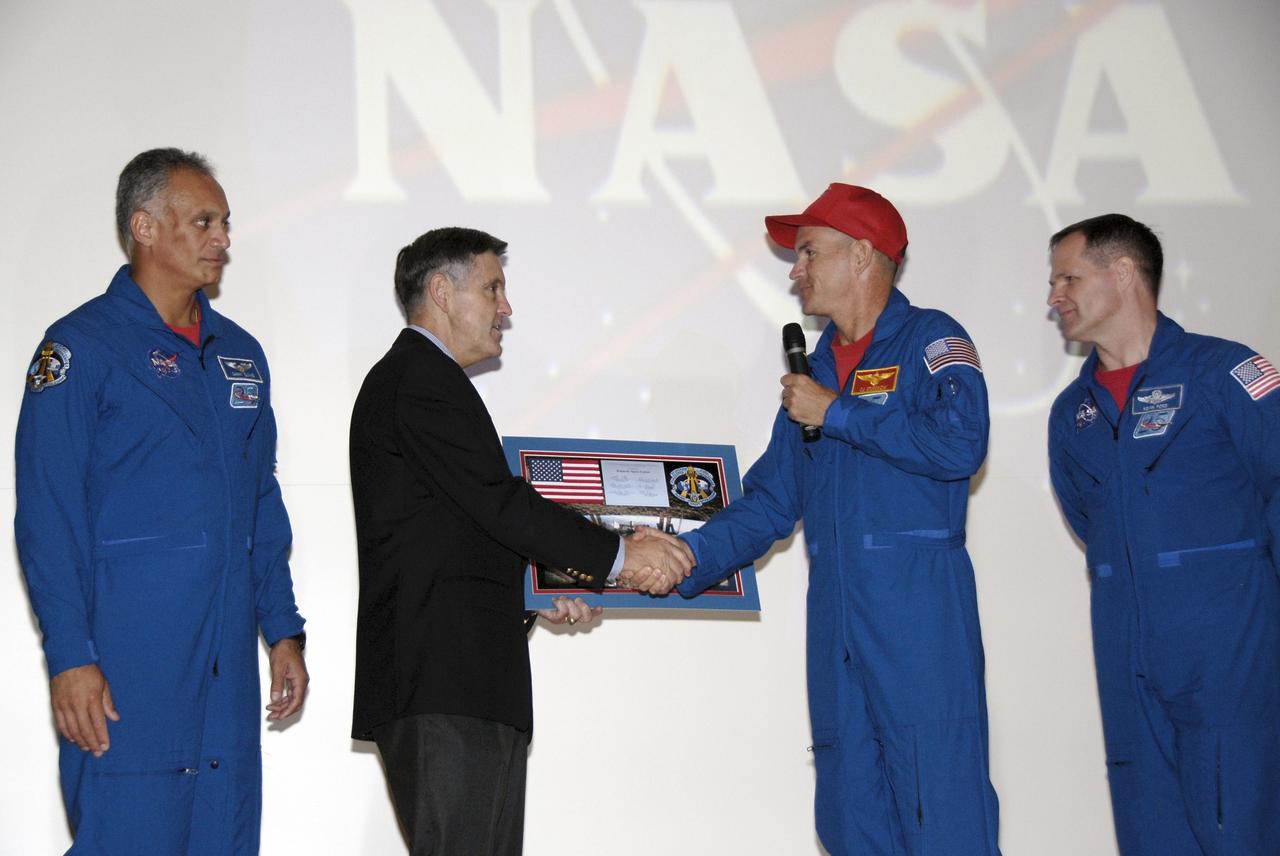 CAPE CANAVERAL, Fla. – In the Training Auditorium at NASA's Kennedy Space Center in Florida, STS-128 Commander Rick Sturckow, with the microphone, presents a plaque commemorating the mission to Center Director Bob Cabana. The presentation followed a program for Kennedy employees in which the crew talked about their experiences on the mission. At left is Mission Specialist John "Danny" Olivas; at right is Pilot Kevin Ford. More than 7 tons of supplies, science racks and equipment, as well as additional environmental hardware to sustain six crew members on the International Space Station were delivered to the International Space Station on the STS-128 mission. The equipment included a freezer to store research samples, a new sleeping compartment and the COLBERT treadmill. The mission was the 128th in the Space Shuttle Program, the 37th flight of Discovery and the 30th station assembly flight. Launch was Aug. 28, 2009. Photo credit: NASA/Kim Shiflett