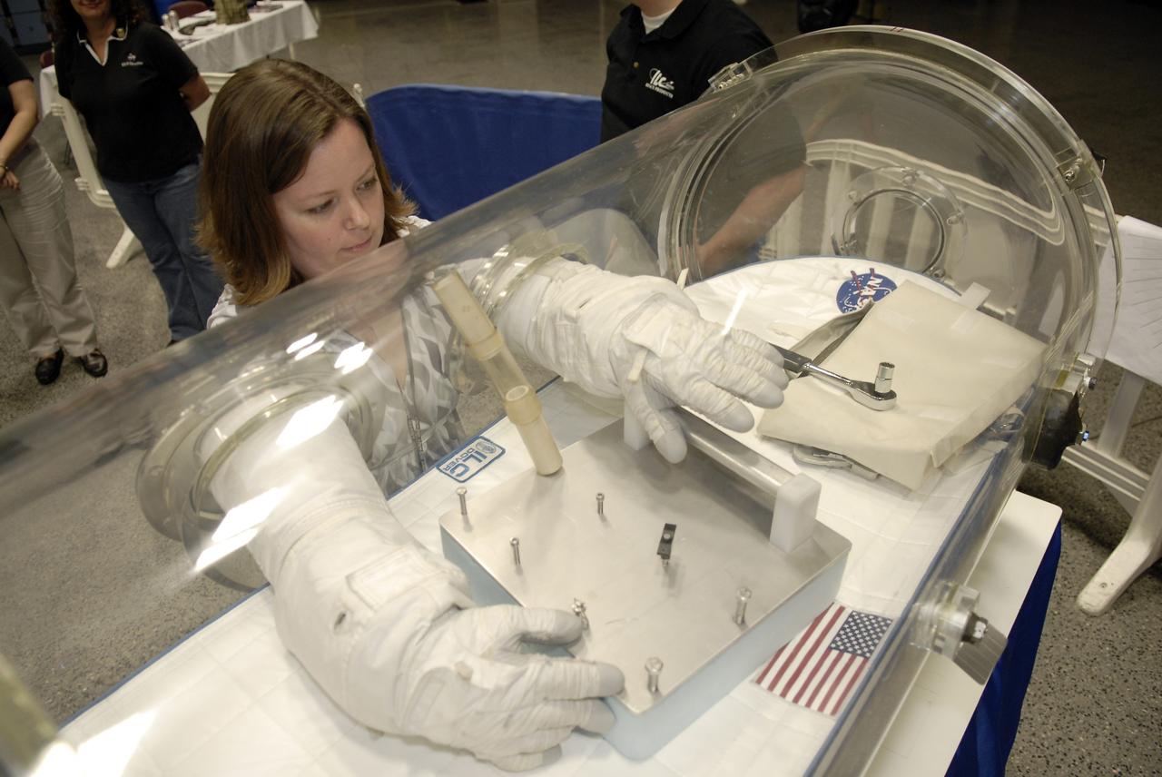 CAPE CANAVERAL, Fla. – At the Astronaut Hall of Fame near NASA’s Kennedy Space Center in Florida, Anna Heiney, a Public Affairs support writer with Abacus Technology at Kennedy, tries out a pair of space gloves for their dexterity and flexibility in a glove box  at the 2009 Astronaut Glove Challenge, part of NASA’s Centennial Challenges Program.  Looking over his shoulder is Kennedy Director Bob Cabana.    The nationwide competition focused on developing improved pressure suit gloves for astronauts to use while working in space.  During the challenge, the gloves were submitted to burst tests, joint force tests and tests to measure their dexterity and strength during operation in a glove box which simulates the vacuum of space.  Centennial Challenges is NASA’s program of technology prizes for the citizen-inventor. The winning prize for the Glove Challenge is $250,000 provided by the Centennial Challenges Program.  Photo credit: NASA/Kim Shiflett