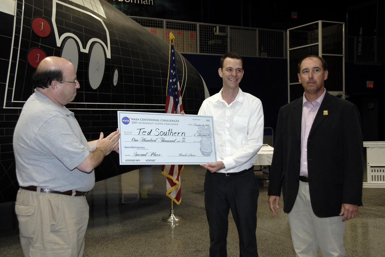 CAPE CANAVERAL, Fla. – Alan Hayes, left, chairman of Volanz Aerospace Inc., presents Ted Southern of Brooklyn, N.Y., with the second place prize of $100,000 at the 2009 Astronaut Glove Challenge, part of NASA’s Centennial Challenges Program, as Andy Petro, manager of NASA Centennial Challenges, stands by at the Astronaut Hall of Fame near NASA’s Kennedy Space Center in Florida.    The nationwide competition focused on developing improved pressure suit gloves for astronauts to use while working in space.  During the challenge, the gloves were submitted to burst tests, joint force tests and tests to measure their dexterity and strength during operation in a glove box which simulates the vacuum of space.  Centennial Challenges is NASA’s program of technology prizes for the citizen-inventor. The winning prize for the Glove Challenge is $250,000 provided by the Centennial Challenges Program.  Photo credit: NASA/Kim Shiflett