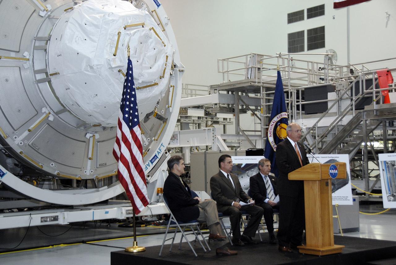 CAPE CANAVERAL, Fla. – In the Space Station Processing Facility at NASA's Kennedy Space Center in Florida, Michael Suffredini, program manager, International Space Station, NASA, addresses the invited guests at a ceremony transferring the ownership of node 3 for the International Space Station, looming in the background, from the European Space Agency, or ESA, to NASA.  Seated, from left, are Michael Suffredini, program manager, International Space Station, NASA; William Dowdell, deputy for Operations, International Space Station and Spacecraft Processing, Kennedy; and Bernardo Patti, head of International Space Station, Program Department, ESA.    Node 3 is named "Tranquility" after the Sea of Tranquility, the lunar landing site of Apollo 11.  The payload for the STS-130 mission, Tranquility is a pressurized module that will provide room for many of the International Space Station's life support systems. The module was built for ESA by Thales Alenia Space in Turin, Italy. Attached to one end of Tranquility is a cupola, a unique work station with six windows on its sides and one on top.  The cupola resembles a circular bay window and will provide a vastly improved view of the station's exterior. Just under 10 feet in diameter, the module will accommodate two crew members and portable workstations that can control station and robotic activities. The multi-directional view will allow the crew to monitor spacewalks and docking operations, as well as provide a spectacular view of Earth and other celestial objects. Space shuttle Endeavour's STS-130 mission is targeted to launch Feb. 4, 2010. Photo credit: NASA/Kim Shiflett