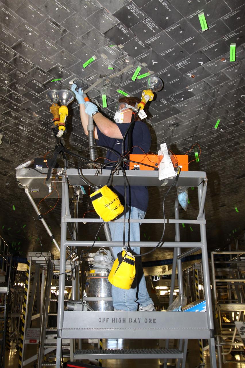 CAPE CANAVERAL, Fla. - In Orbiter Processing Facility Bay 1 at NASA's Kennedy Space Center in Florida, United Space Alliance technician Jeff Holmes uses heat lamps in a putty repair on some of the high-temperature reusable surface insulation tiles, or HRSI tiles, on the lower forward fuselage of space shuttle Atlantis. An average of 125 tiles are replaced after each mission either due to handling damage or accumulated repairs. These black tiles are optimized for maximum emissivity, which means they lose heat faster than white tiles. This property is required to maximize heat rejection during the hot phase of reentry. Atlantis next is slated to deliver an Integrated Cargo Carrier and Russian-built Mini Research Module to the International Space Station on the STS-132 mission. Launch is targeted for May 14, 2010. Photo credit: NASA/Jack Pfaller