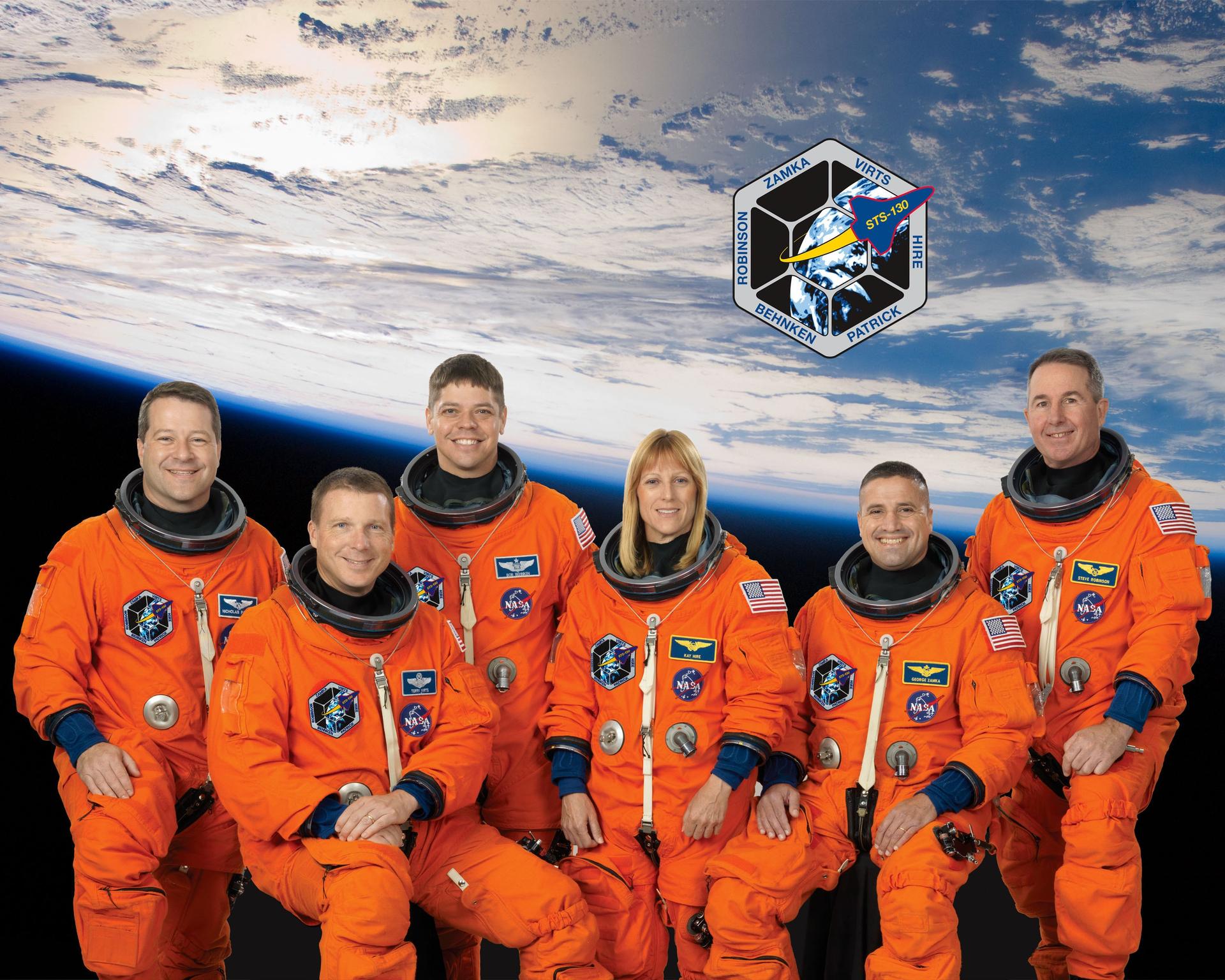 Attired in training versions of their shuttle launch and entry suits, these six astronauts take a break from training to pose for the STS-130 crew portrait in orange spacesuits with earth and mission patch in the background.
