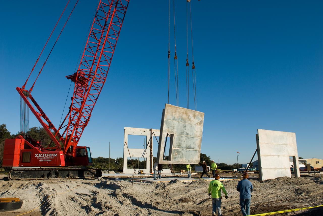 CAPE CANAVERAL, Fla. - In Launch Complex 39 at NASA's Kennedy Space Center in Florida, workers guide one of the walls of the Propellants North Administrative and Maintenance Facility into place.    A tilt-up construction method is being used to erect a THERMOMASS concrete wall insulation system for the facility's walls.  In this approach, the exterior layer of concrete for the wall panels is poured and leveled on the building's footprint. Then, prefabricated, predrilled insulation sheets are arranged on top of the unhardened concrete, and connectors, designed to hold the sandwiched layers of concrete and insulation secure, are inserted through the predrilled holes. Next, the structural wythe is poured.  Once cured, these panels are lifted upright to form the building's envelope.  The facility will have a two-story administrative building to house managers, mechanics and technicians who fuel spacecraft at Kennedy adjacent to an 1,800-square-foot single-story shop to store cryogenic fuel transfer equipment.  The new facility will feature high-efficiency roofs and walls, “Cool Dry Quiet” air conditioning with energy recovery technology, efficient lighting, and other sustainable features. The facility is striving to qualify for the U.S. Green Building Council’s Leadership in Energy and Environmental Design, or LEED, Platinum certification. If successful, Propellants North will be the first Kennedy facility to achieve this highest of LEED ratings after it is completed in the summer of 2010.  The facility was designed for NASA by Jones Edmunds and Associates.  Photo credit: NASA/Jim Grossmann