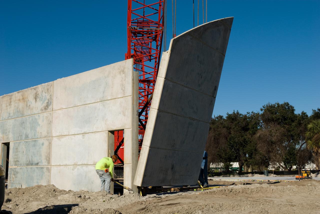 CAPE CANAVERAL, Fla. - In Launch Complex 39 at NASA's Kennedy Space Center in Florida, the Propellants North Administrative and Maintenance Facility begins to take shape as its walls are lifted into position.    A tilt-up construction method is being used to erect a THERMOMASS concrete wall insulation system for the facility's walls.  In this approach, the exterior layer of concrete for the wall panels is poured and leveled on the building's footprint. Then, prefabricated, predrilled insulation sheets are arranged on top of the unhardened concrete, and connectors, designed to hold the sandwiched layers of concrete and insulation secure, are inserted through the predrilled holes. Next, the structural wythe is poured.  Once cured, these panels are lifted upright to form the building's envelope.  The facility will have a two-story administrative building to house managers, mechanics and technicians who fuel spacecraft at Kennedy adjacent to an 1,800-square-foot single-story shop to store cryogenic fuel transfer equipment.  The new facility will feature high-efficiency roofs and walls, “Cool Dry Quiet” air conditioning with energy recovery technology, efficient lighting, and other sustainable features. The facility is striving to qualify for the U.S. Green Building Council’s Leadership in Energy and Environmental Design, or LEED, Platinum certification. If successful, Propellants North will be the first Kennedy facility to achieve this highest of LEED ratings after it is completed in the summer of 2010.  The facility was designed for NASA by Jones Edmunds and Associates.  Photo credit: NASA/Jim Grossmann