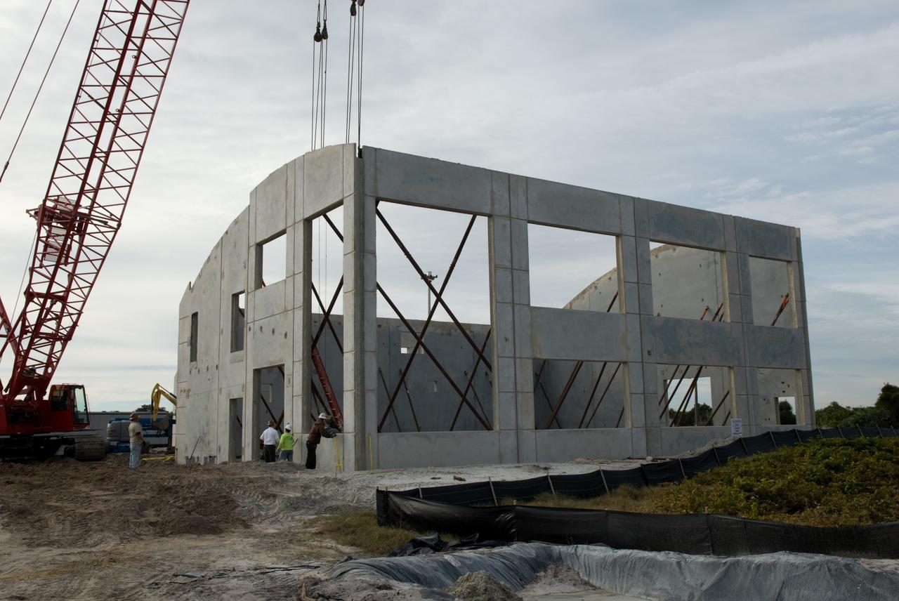 CAPE CANAVERAL, Fla. - In Launch Complex 39 at NASA's Kennedy Space Center in Florida, construction workers survey the last outside wall of the Propellants North Administrative and Maintenance Facility.    Concrete layers on either side of high-density foam insulation in the facility's walls will prevent any transfer of radiant heat between the exterior and interior of the buildings.  A tilt-up construction method is being used to erect a THERMOMASS concrete wall insulation system for the facility's walls.  In this approach, the exterior layer of concrete for the wall panels is poured and leveled on the building's footprint. Then, prefabricated, predrilled insulation sheets are arranged on top of the unhardened concrete, and connectors, designed to hold the sandwiched layers of concrete and insulation secure, are inserted through the predrilled holes. Next, the structural wythe is poured.  Once cured, these panels are lifted upright to form the building's envelope.  The facility will have a two-story administrative building to house managers, mechanics and technicians who fuel spacecraft at Kennedy adjacent to an 1,800-square-foot single-story shop to store cryogenic fuel transfer equipment.  The new facility will feature high-efficiency roofs and walls, “Cool Dry Quiet” air conditioning with energy recovery technology, efficient lighting, and other sustainable features. The facility is striving to qualify for the U.S. Green Building Council’s Leadership in Energy and Environmental Design, or LEED, Platinum certification. If successful, Propellants North will be the first Kennedy facility to achieve this highest of LEED ratings after it is completed in the summer of 2010.  The facility was designed for NASA by Jones Edmunds and Associates.  Photo credit: NASA/Jim Grossmann