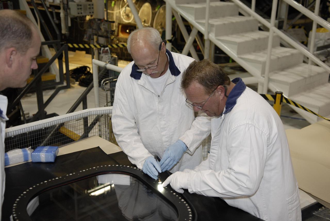 CAPE CANAVERAL, Fla. - In Orbiter Processing Facility 1 at NASA's Kennedy Space Center in Florida, United Space Alliance technicians discuss the condition of window #8, removed from the top of space shuttle Atlantis' crew module for inspection.     Inspection and maintenance of the crew module windows is standard procedure between shuttle missions.  Atlantis is next slated to deliver an Integrated Cargo Carrier and Russian-built Mini Research Module to the International Space Station on the STS-132 mission.  The second in a series of new pressurized components for Russia, the module will be permanently attached to the Zarya module. Three spacewalks are planned to store spare components outside the station, including six spare batteries, a boom assembly for the Ku-band antenna and spares for the Canadian Dextre robotic arm extension. A radiator, airlock and European robotic arm for the Russian Multi-purpose Laboratory Module also are payloads on the flight.  Launch is targeted for May 14.  Photo credit: NASA/Glenn Benson