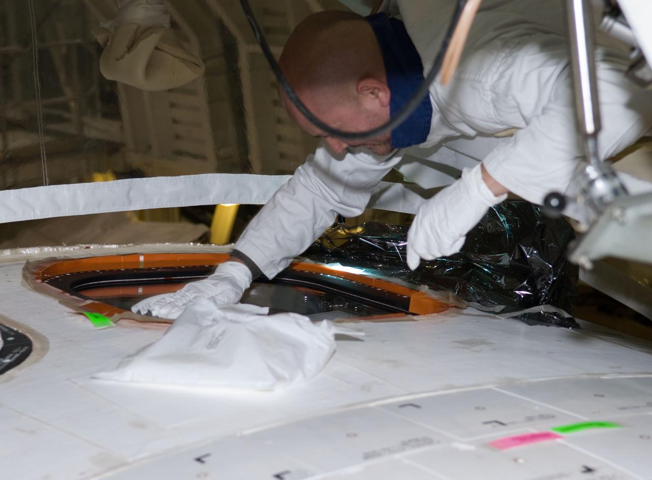 CAPE CANAVERAL, Fla. - In Orbiter Processing Facility 1 at NASA's Kennedy Space Center in Florida, a United Space Alliance technician working on the top of space shuttle Atlantis' crew module checks the placement of newly installed window #8.     Inspection and maintenance of the crew module windows is standard procedure between shuttle missions.  Atlantis is next slated to deliver an Integrated Cargo Carrier and Russian-built Mini Research Module to the International Space Station on the STS-132 mission.  The second in a series of new pressurized components for Russia, the module will be permanently attached to the Zarya module. Three spacewalks are planned to store spare components outside the station, including six spare batteries, a boom assembly for the Ku-band antenna and spares for the Canadian Dextre robotic arm extension. A radiator, airlock and European robotic arm for the Russian Multi-purpose Laboratory Module also are payloads on the flight.  Launch is targeted for May 14.  Photo credit: NASA/Jim Grossmann