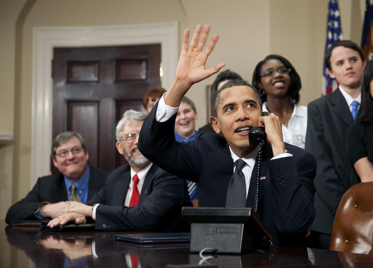 WASHINGTON - 201002170001HQ - U.S. President Barack Obama, accompanied by members of Congress and middle school children, waves as he talks on the phone from the Roosevelt Room of the White House to astronauts on the International Space Station, Wednesday, Feb. 17, 2010, in Washington. Photo Credit: NASA/Bill Ingalls