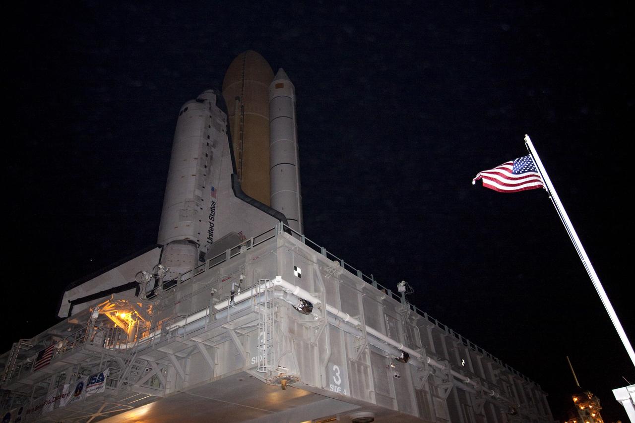 CAPE CANAVERAL, Fla. -- At NASA's Kennedy Space Center in Florida, the American flag is illuminated next to space shuttle Discovery as the spacecraft makes the last leg of its journey, known as "rollout," from the Vehicle Assembly Building to Launch Pad 39A. It took the shuttle, attached to its external fuel tank, twin solid rocket boosters and mobile launcher platform, about six hours to complete the move atop a crawler-transporter. Rollout sets the stage for Discovery's STS-133 crew to practice countdown and launch procedures during the Terminal Countdown Demonstration Test in mid-October. Targeted to liftoff Nov. 1, Discovery will take the Permanent Multipurpose Module (PMM) packed with supplies and critical spare parts, as well as Robonaut 2 (R2) to the International Space Station. Photo credit: NASA/Jack Pfaller