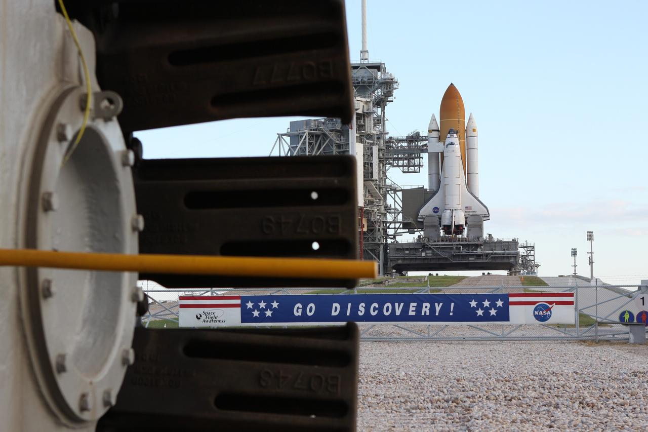 CAPE CANAVERAL, Fla. -- At NASA's Kennedy Space Center in Florida, the STS-133 payload canister now is in the rotating service structure on Launch Pad 39A. A sign hanging on the fence in front of the pad entrance supporting space shuttle Discovery is seen through the tred from a crawler-transporter.      The payload then will be moved into space shuttle Discovery's payload bay. Discovery and its STS-133 crew will deliver the Permanent Multipurpose Module, packed with supplies and critical spare parts, as well as Robonaut 2, the dexterous humanoid astronaut helper, to the International Space Station. Launch is targeted for 4:40 p.m. EDT, Nov. 1. Photo credit: NASA/Troy Cryder