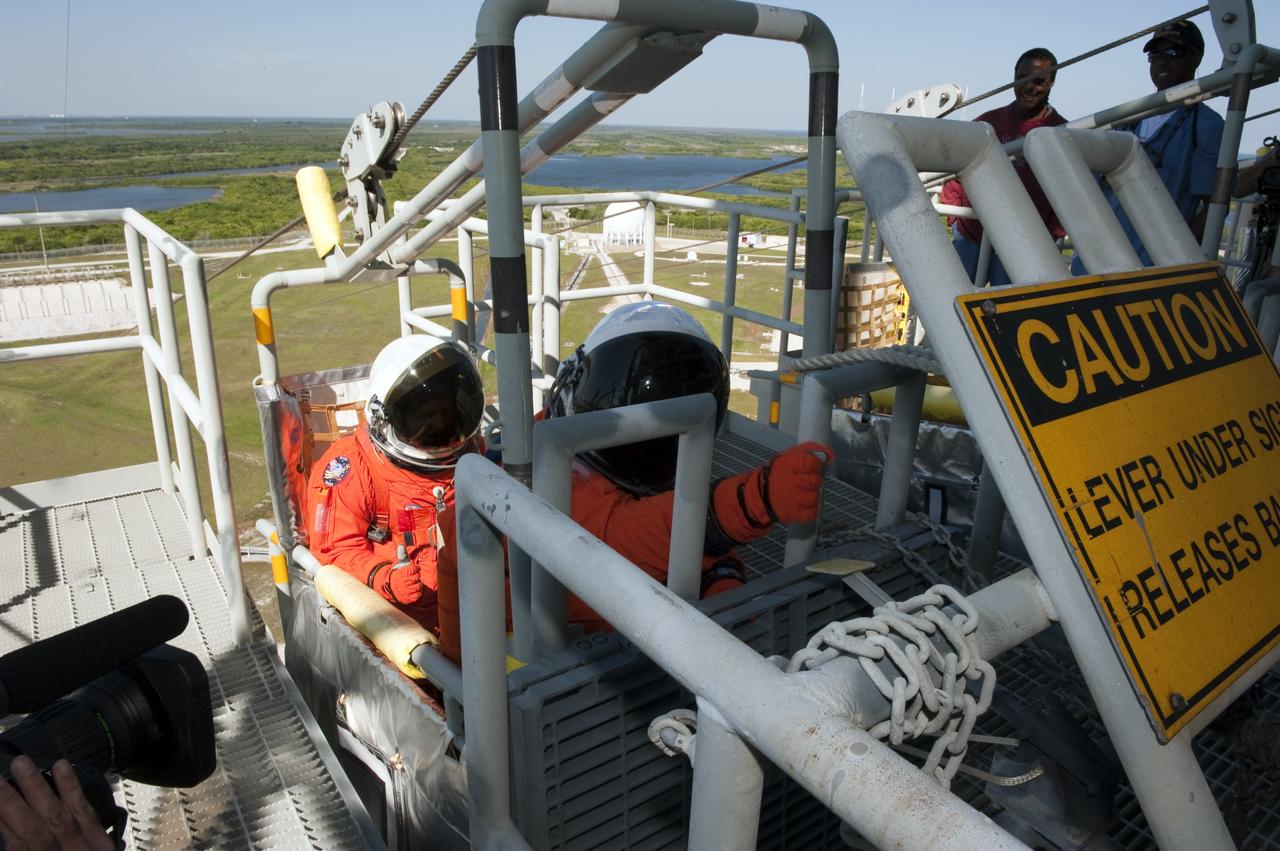CAPE CANAVERAL, Fla. -- During a simulated pad emergency on Launch Pad 39A at NASA's Kennedy Space Center in Florida, STS-133 Mission Specialists Tim Kopra, left, and Alvin Drew hop in a slidewire basket that would take them to a safe bunker below the pad in an unlikely emergency situation. The emergency training while aboard space shuttle Discovery is part of a week-long Terminal Countdown Demonstration Test (TCDT). Discovery and its STS-133 crew will deliver the Permanent Multipurpose Module, packed with supplies and critical spare parts, as well as Robonaut 2, the dexterous humanoid astronaut helper, to the International Space Station. Launch is targeted for Nov. 1 at 4:40 p.m. For more information on the STS-133 mission, visit www.nasa.gov/mission_pages/shuttle/shuttlemissions/sts133/. Photo credit: NASA/Kim Shiflett